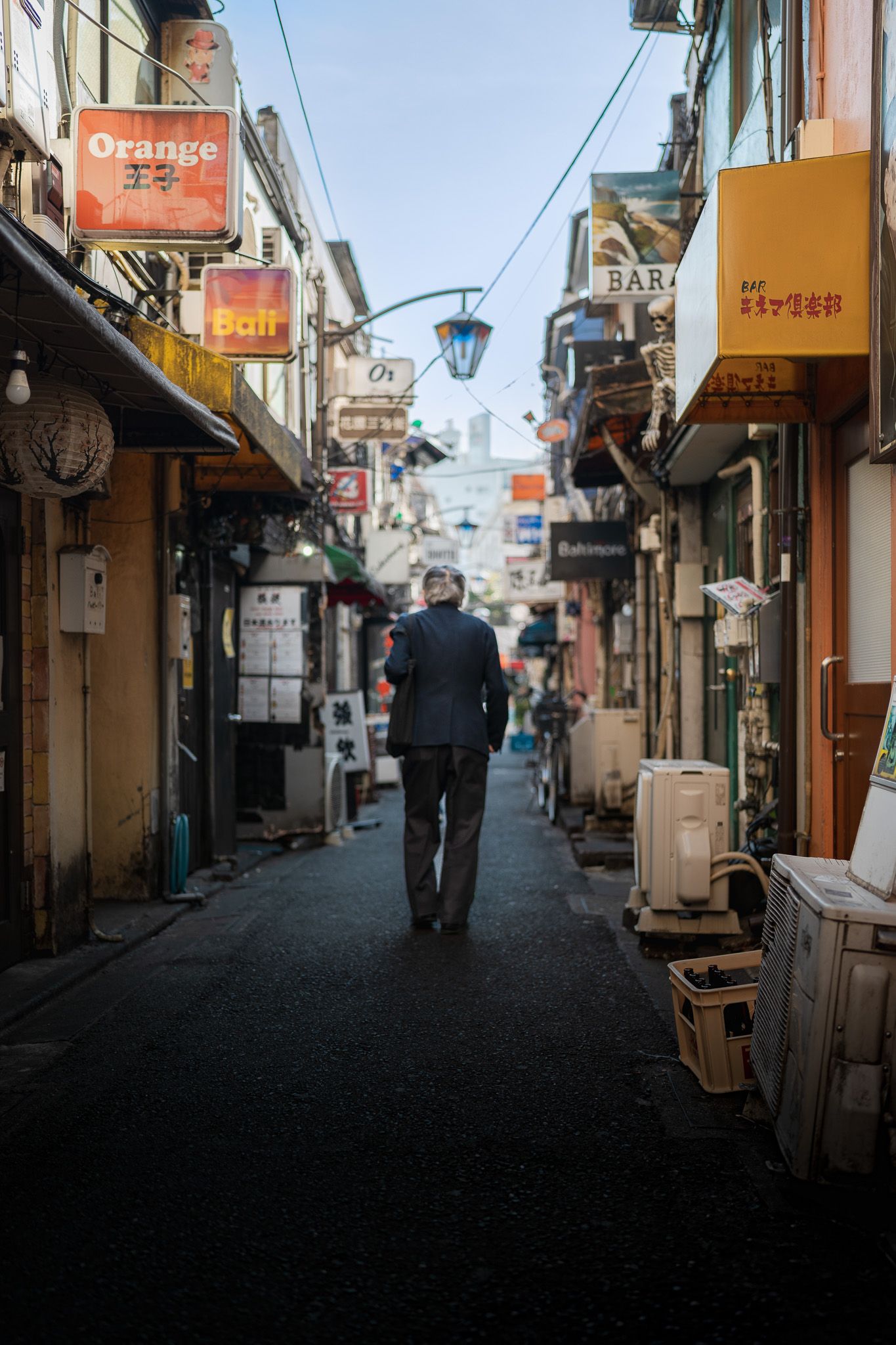 travel photo of tokyo, japan where old man is walking down vibrant alleyway full of signs in orange