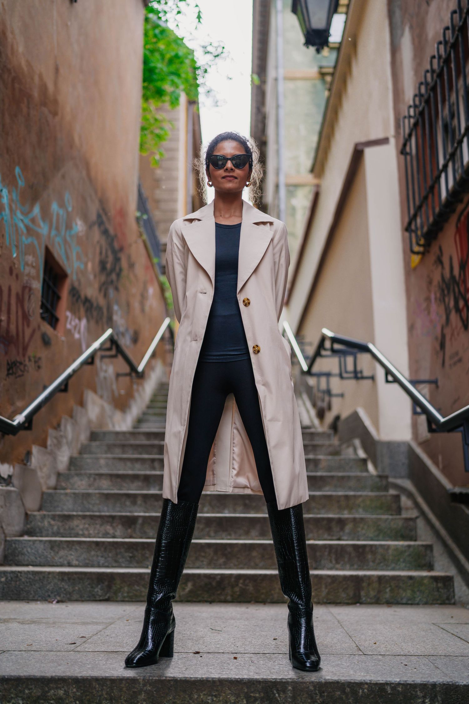 portrait of woman dressed in a trench coat and boots standing powerfully in colorful warsaw alley way