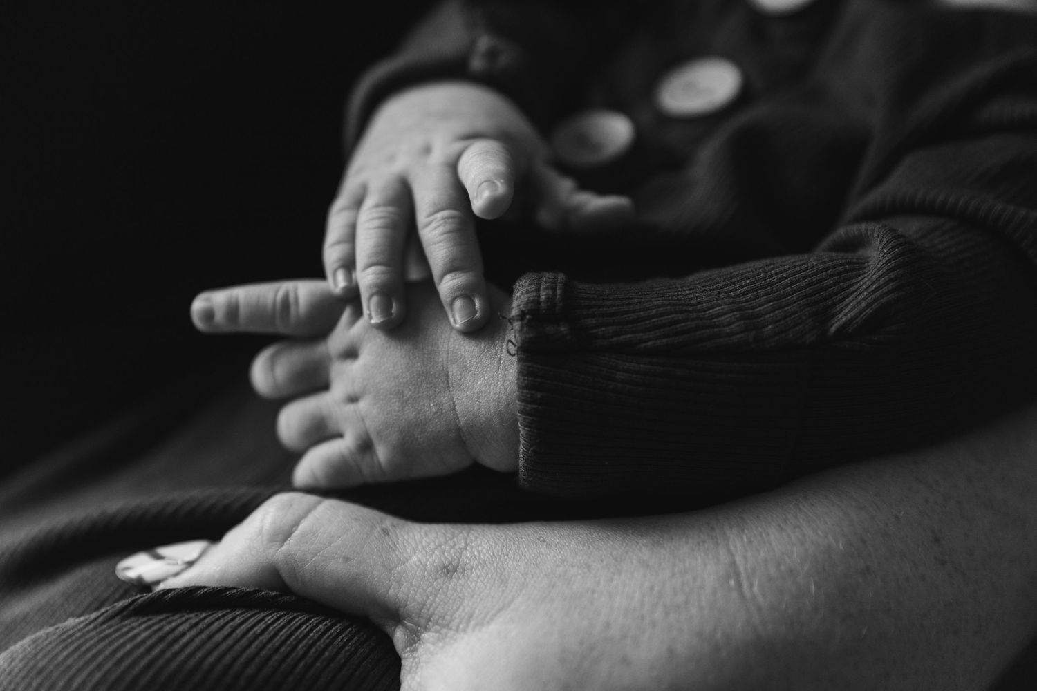 A black and white close-up photograph of small hands gently resting on larger hands in an intimate moment.
