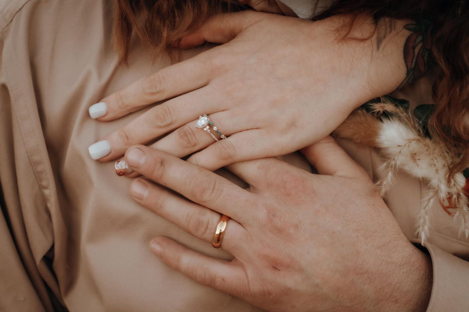 Close-up of hands wearing wedding rings against neutral background.