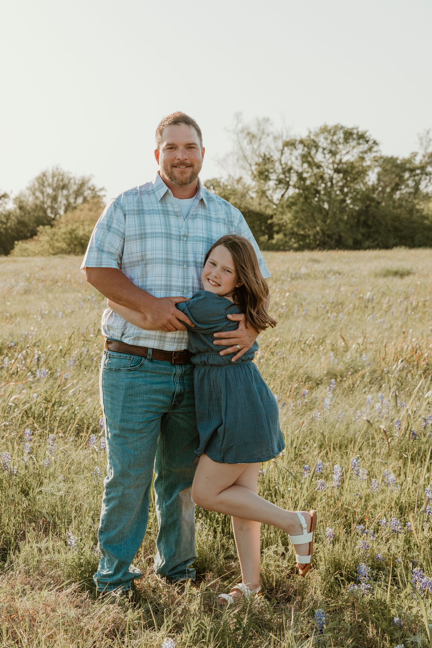 Family wearing coordinating blue outfits poses together in flowering meadow at golden hour.