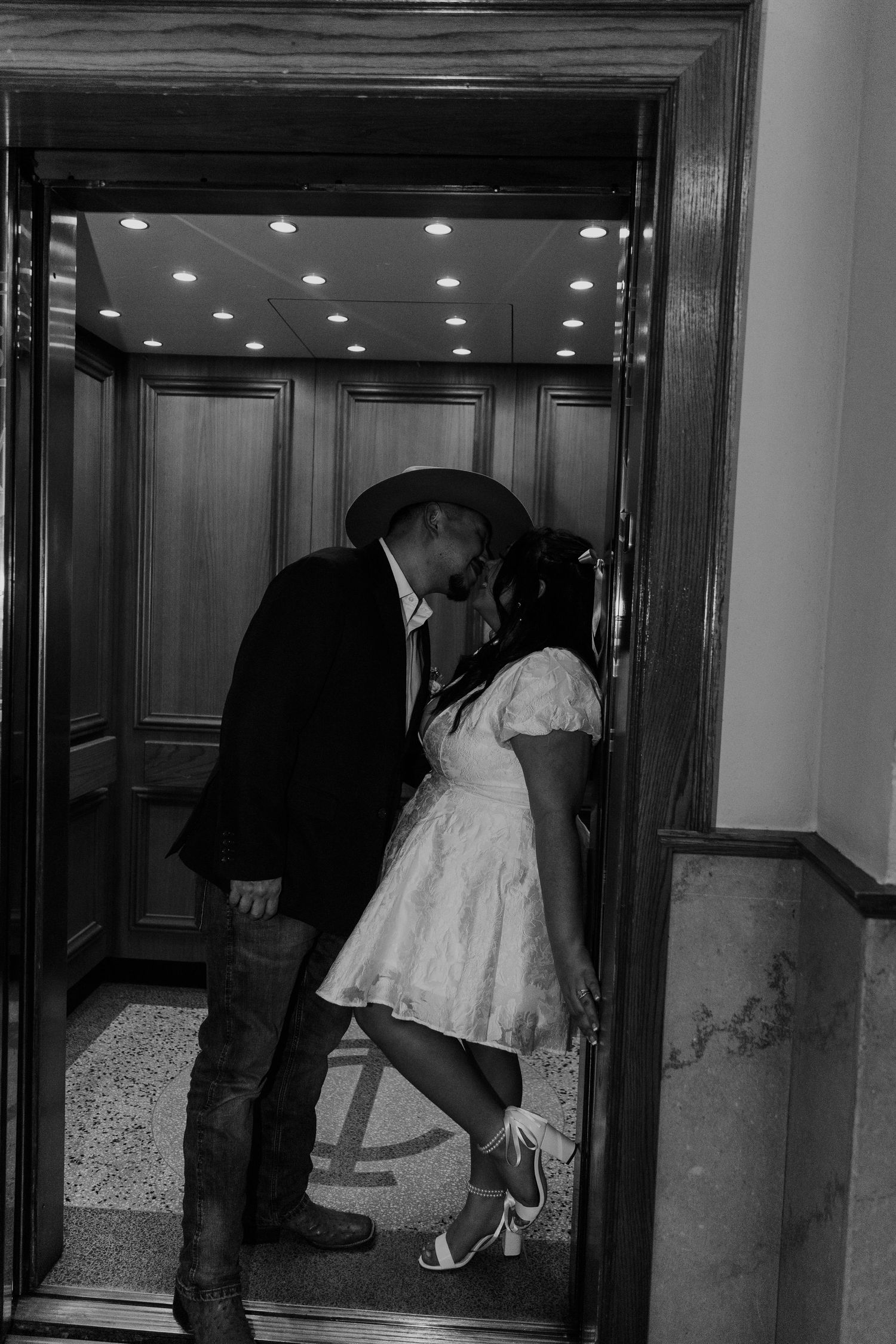 Couple in formal attire sharing intimate moments in a dimly lit elevator.