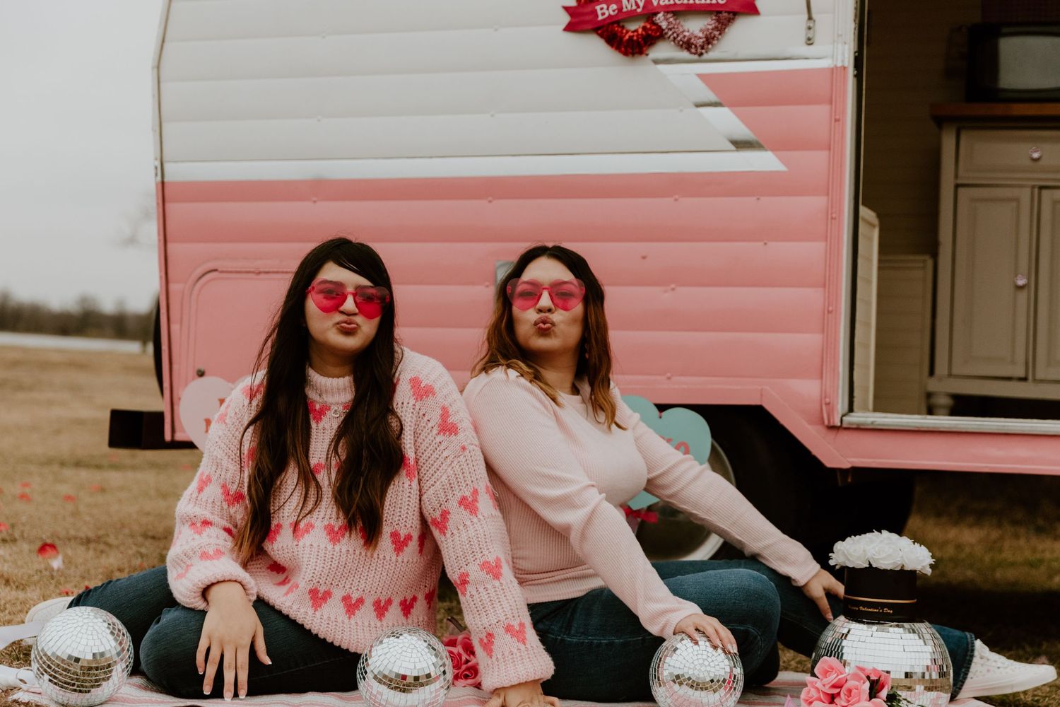 Friends enjoying retro-style Valentine's photoshoot near pink vintage camper.