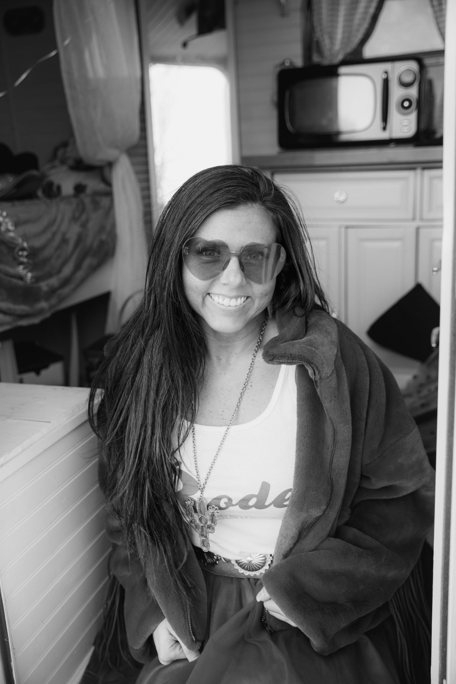 Woman wearing sunglasses and oversized jacket poses in black and white photo.