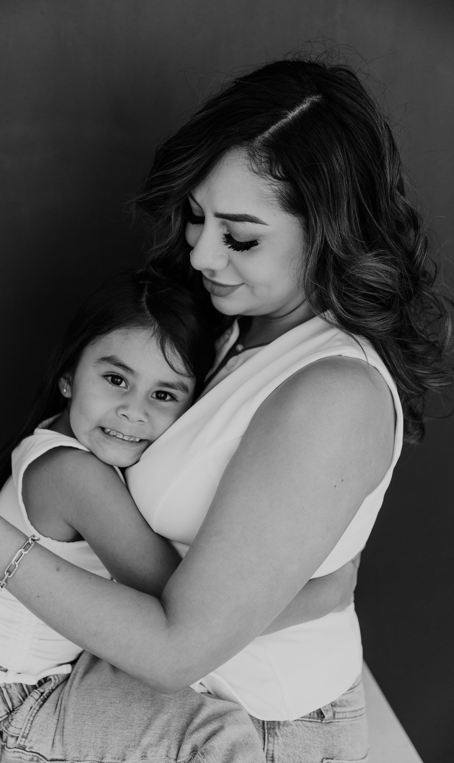 Black and white portrait of parent and child embracing against dark background.