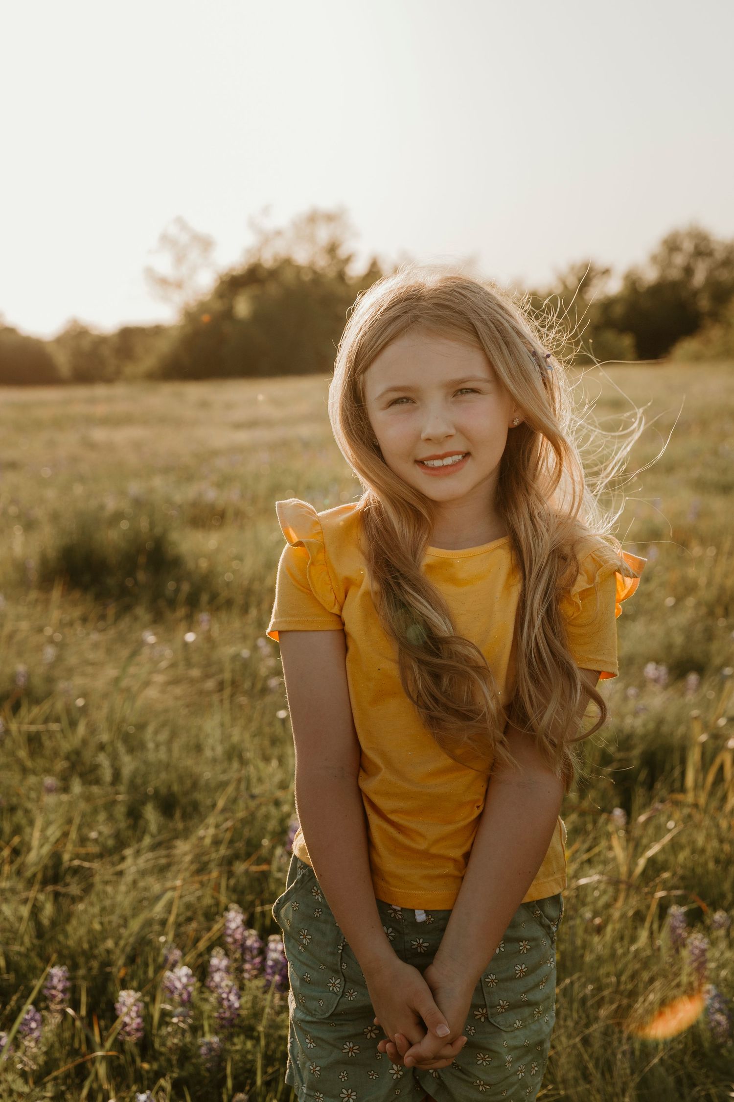 Sunset portrait in field wearing yellow t-shirt surrounded by purple wildflowers.