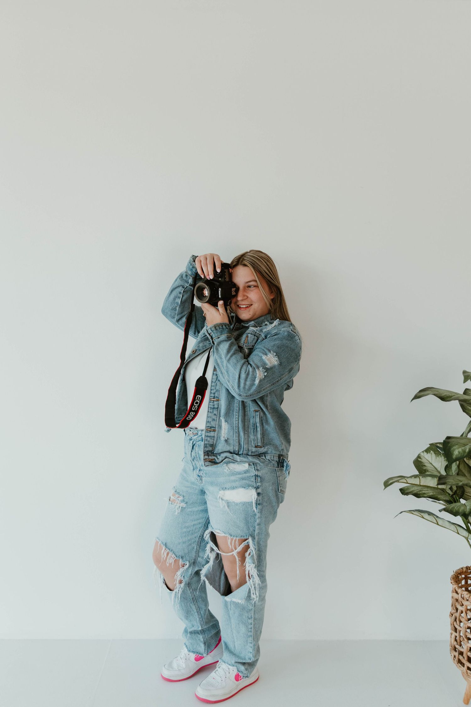 Person in double denim outfit taking photos with professional camera in studio setting with plant.