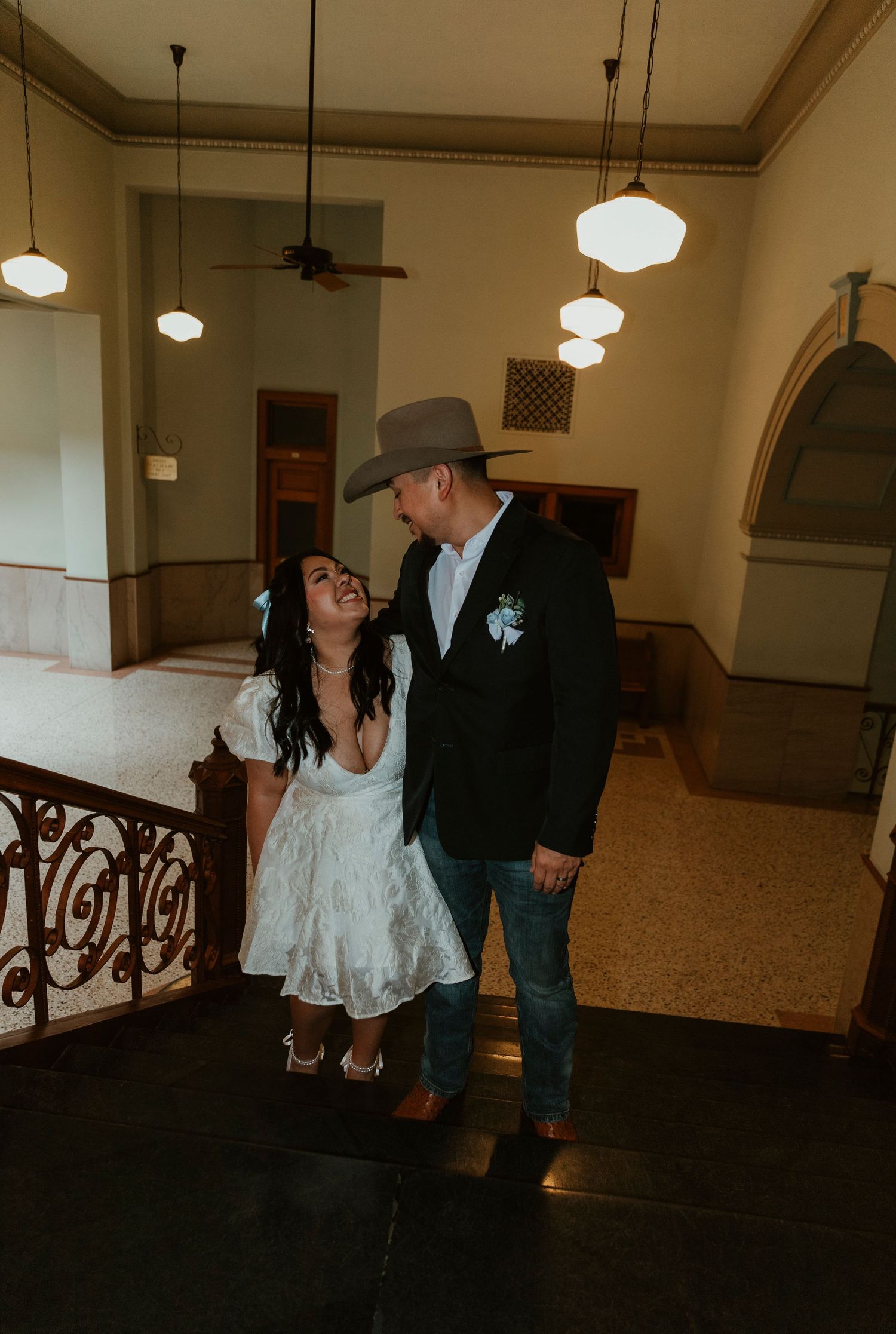 Romantic scene in a vintage building interior with ornate railings and pendant lighting.