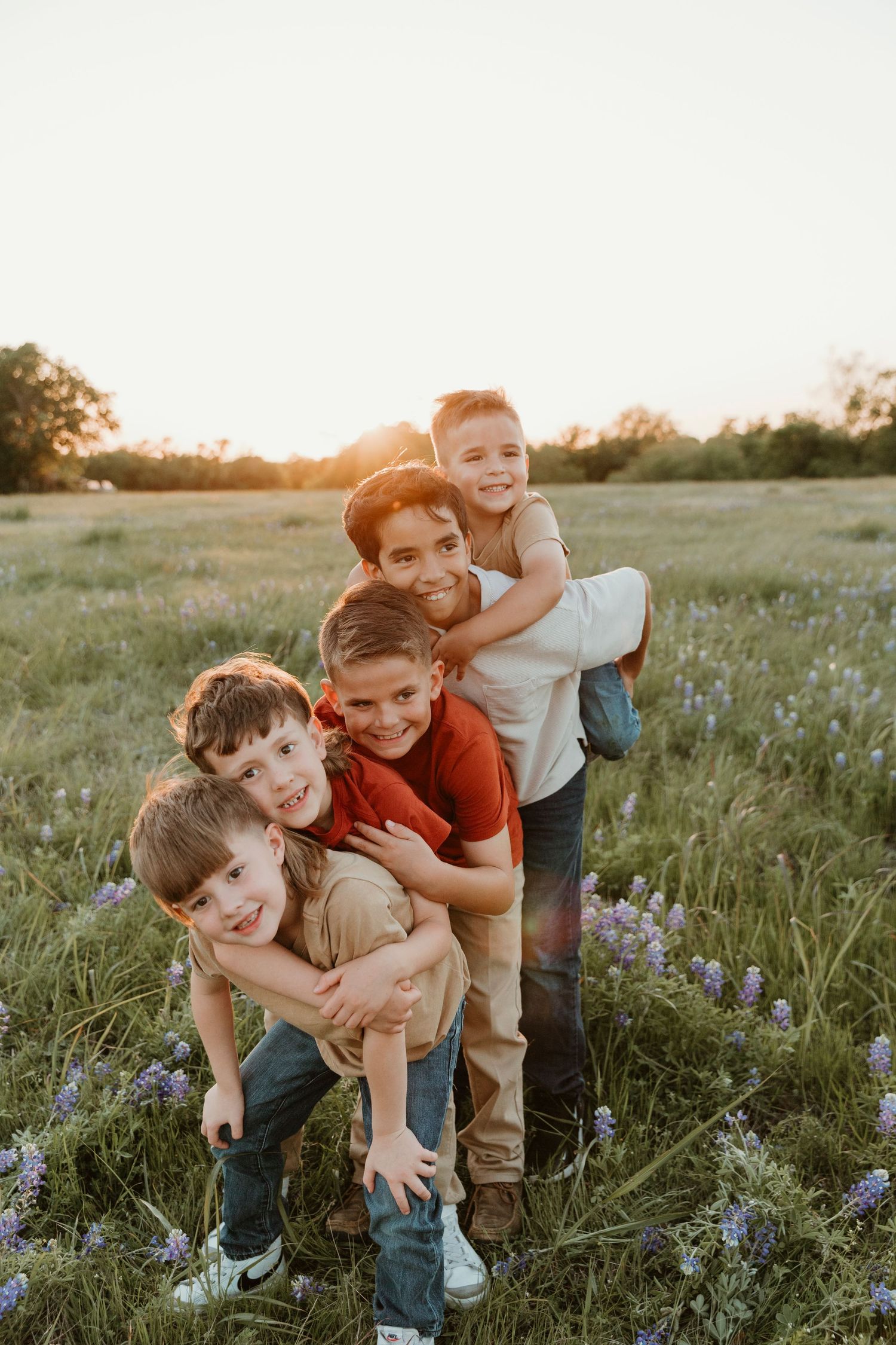 Playful children giving piggyback rides in a field of wildflowers during sunset.