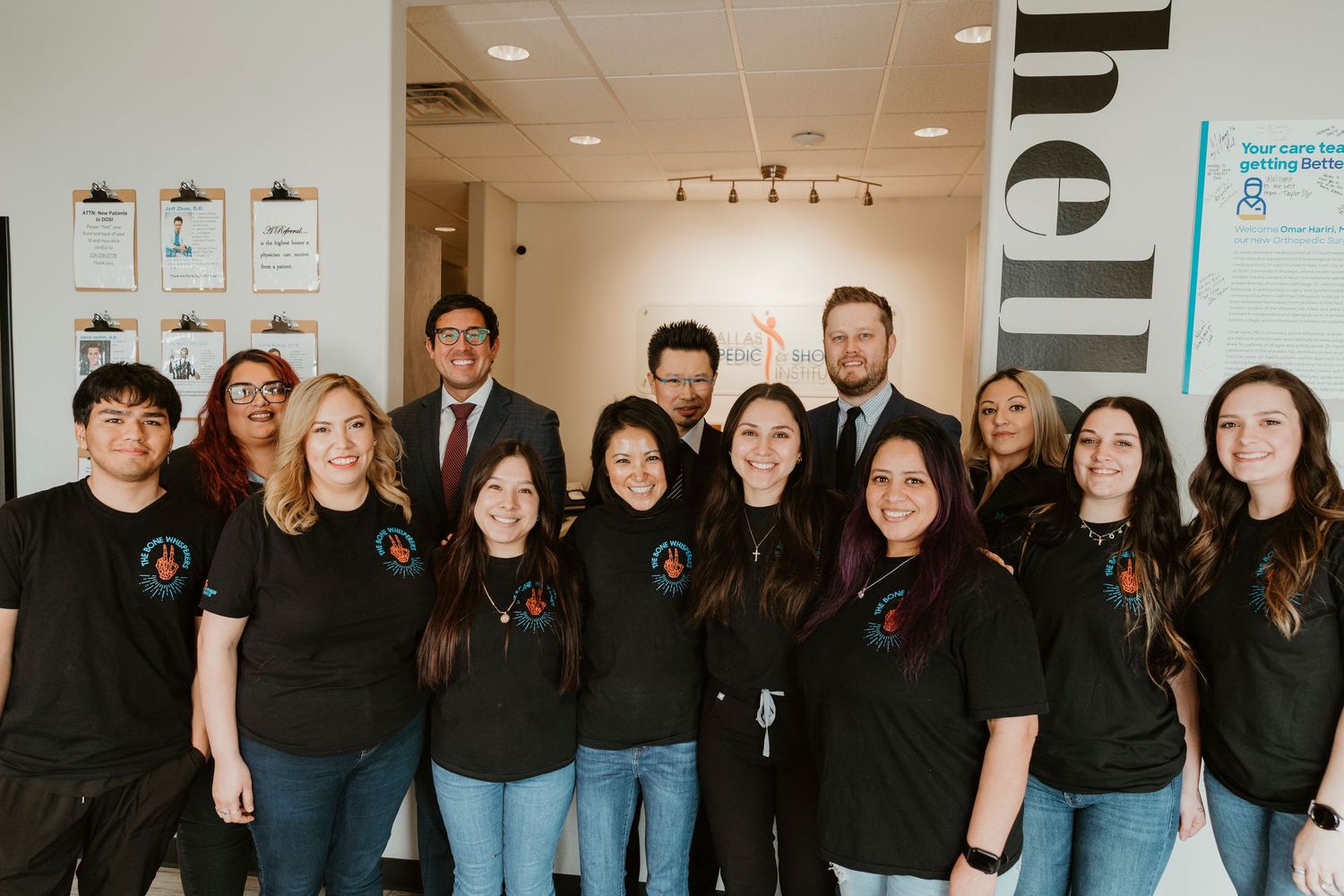 Group photo of team members wearing matching black polo shirts in office hallway.