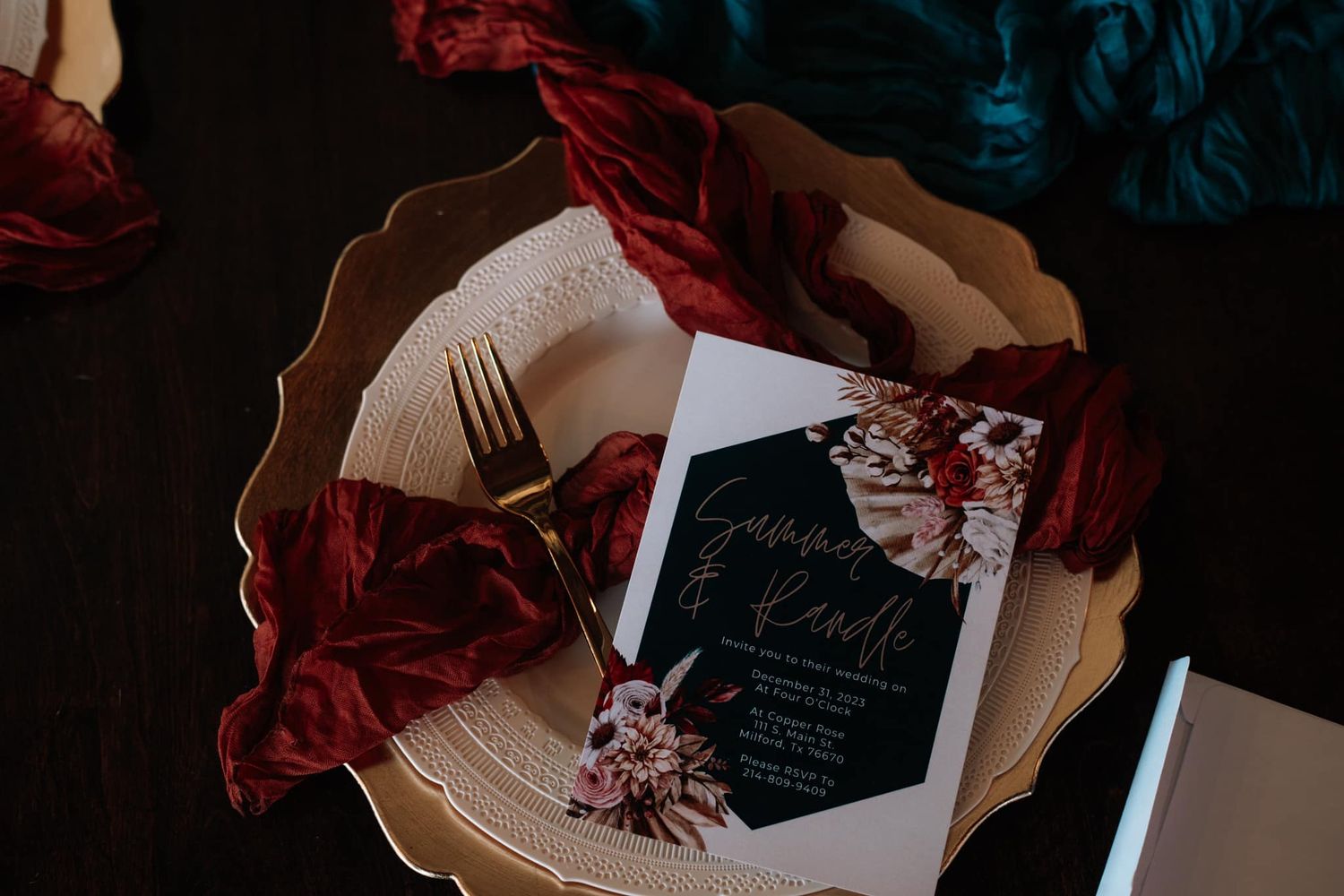 Wedding invitation on ornate plate with burgundy decor elements against dark background.