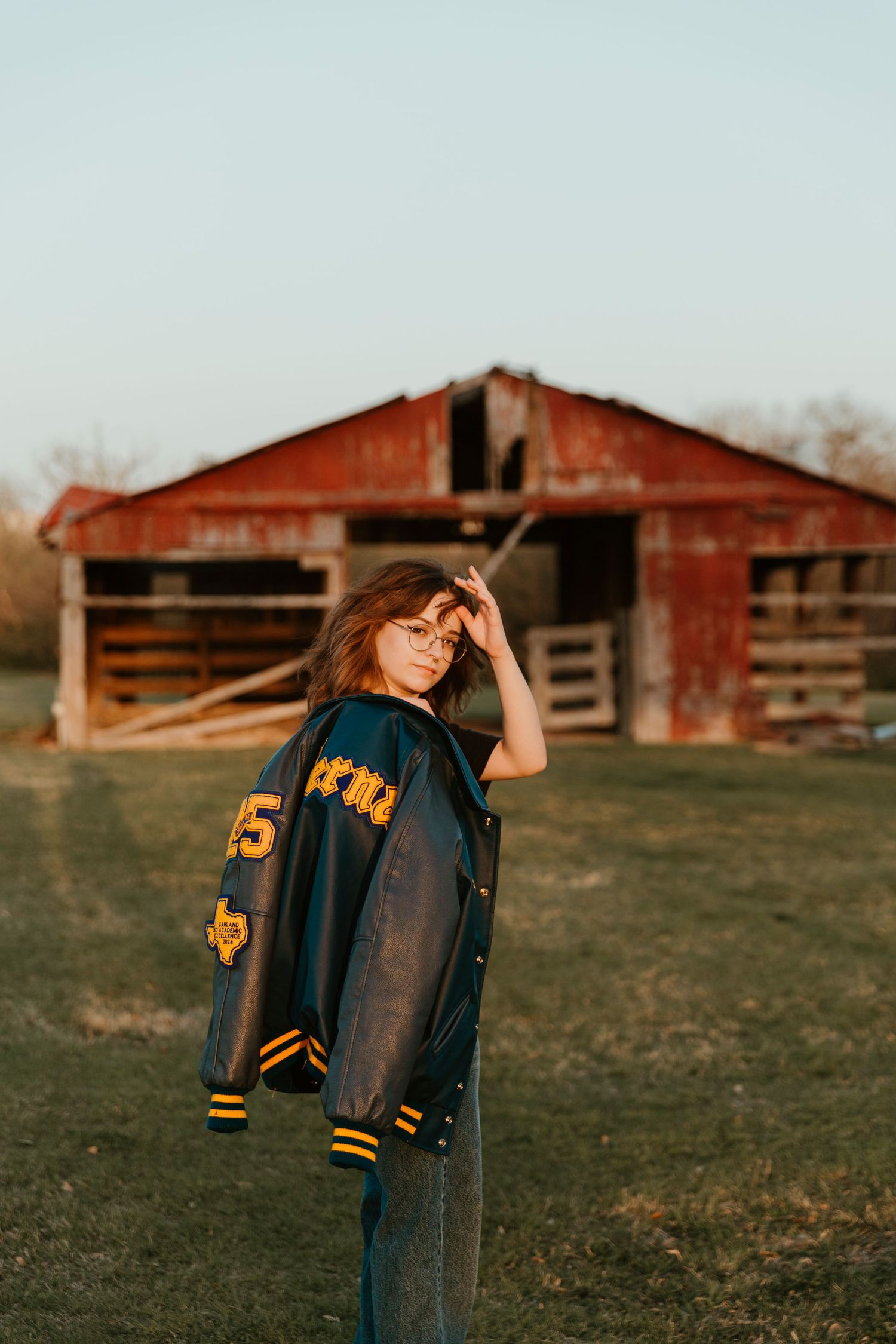 A vintage letterman jacket posed against a red barn in soft evening light.