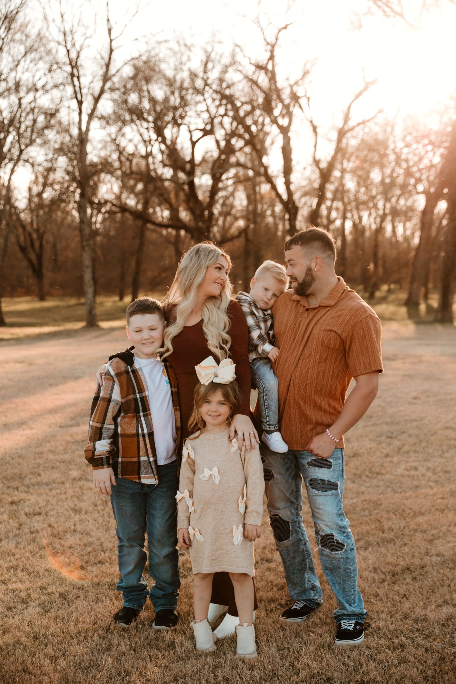 A family stands together in a golden-lit field at sunset wearing coordinated casual fall outfits.