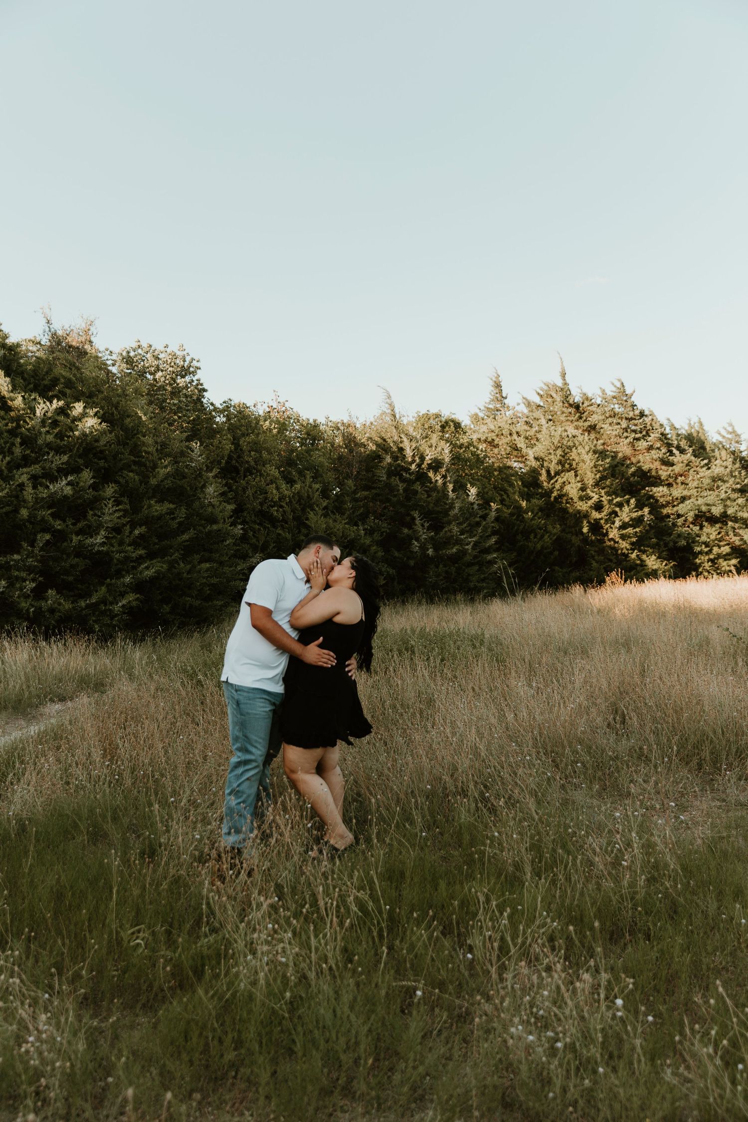 Couple embracing in a serene meadow with tall grass at sunset, captured in a romantic photoshoot series.