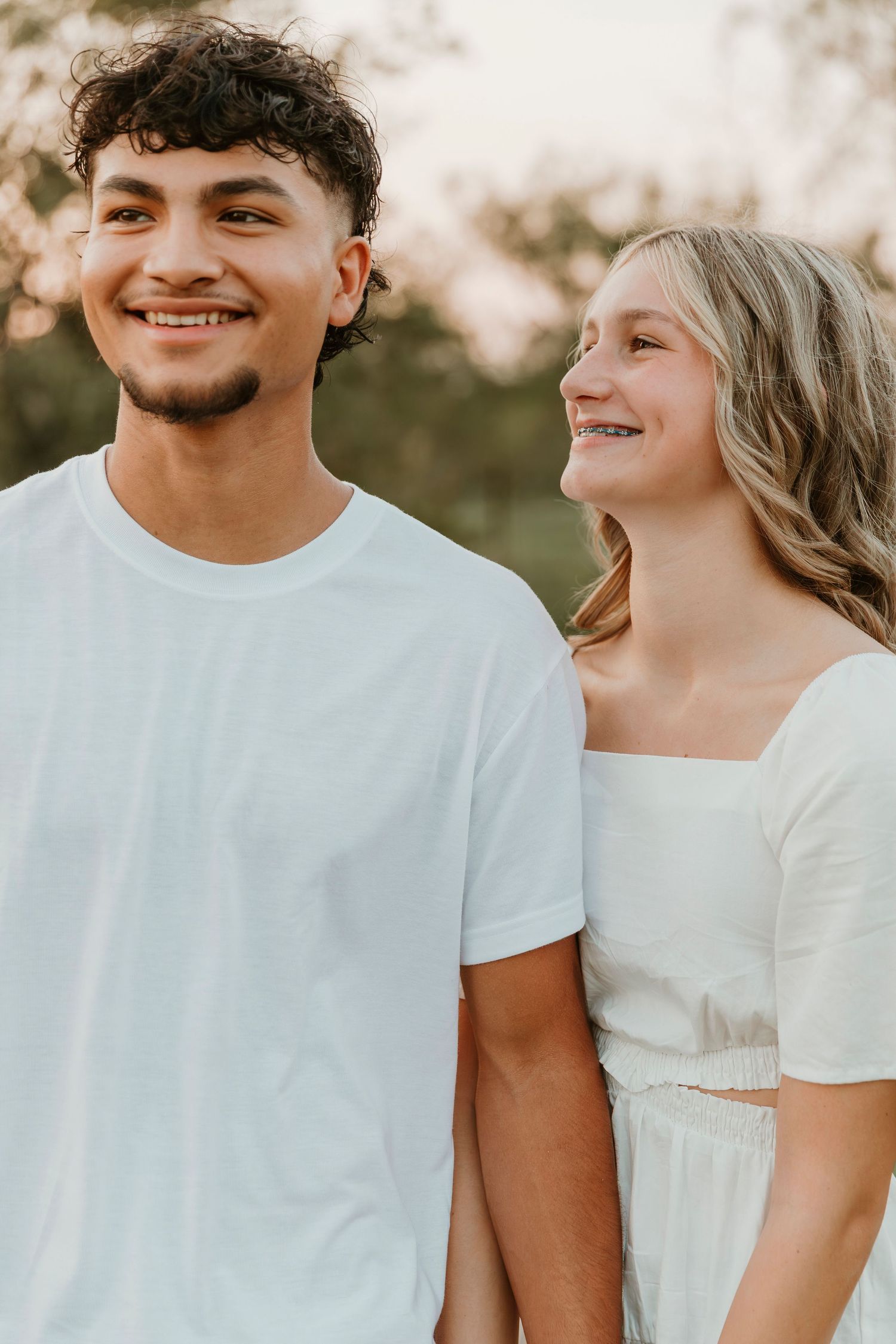 A couple in white outfits smiling together during a sunset photoshoot.