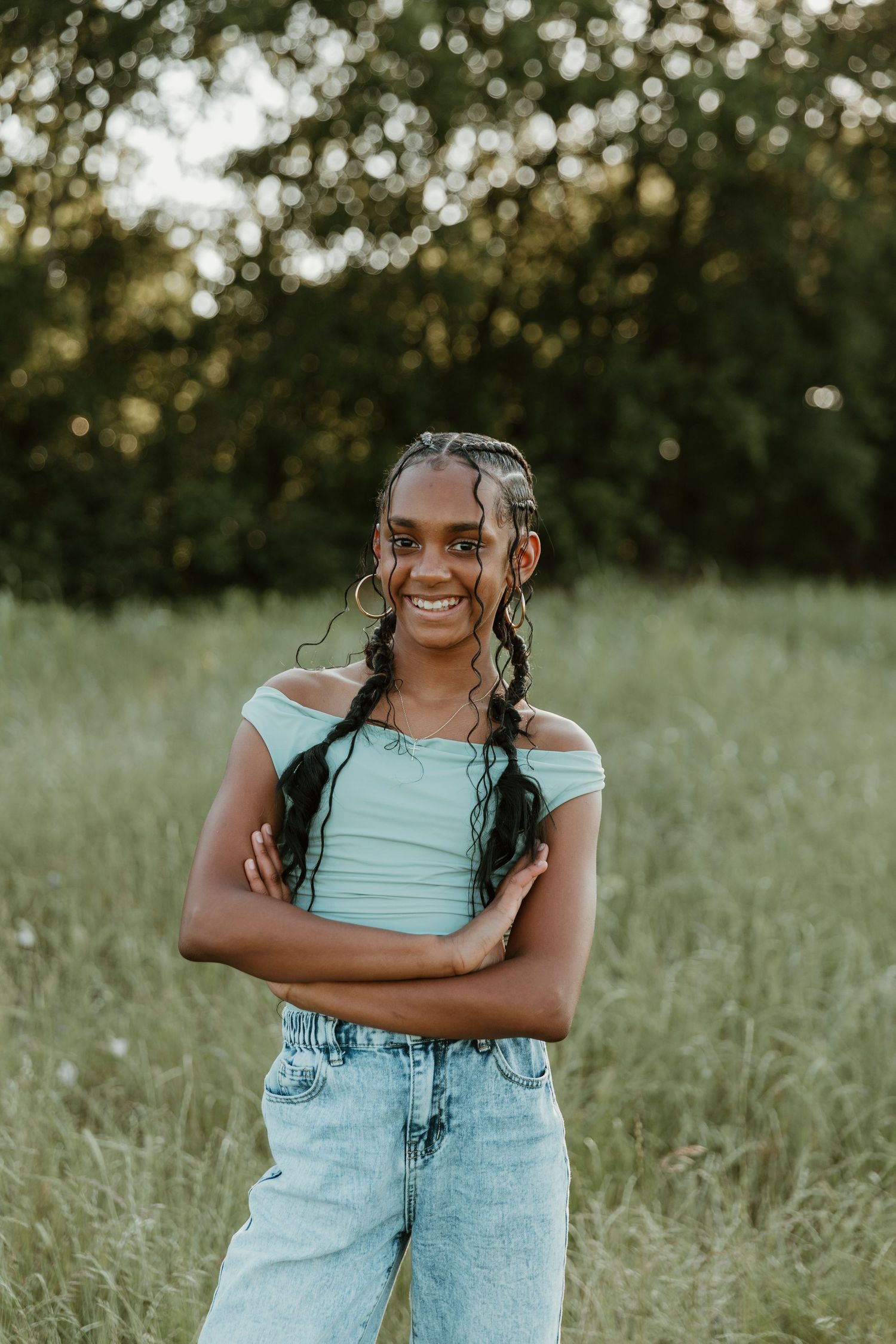 A candid portrait in a grassy field shows a bright smile and braided hairstyle.