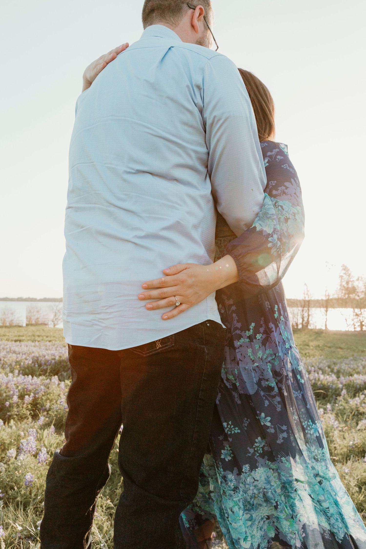Side view of couple embracing in turquoise dress and grey shirt at sunset.