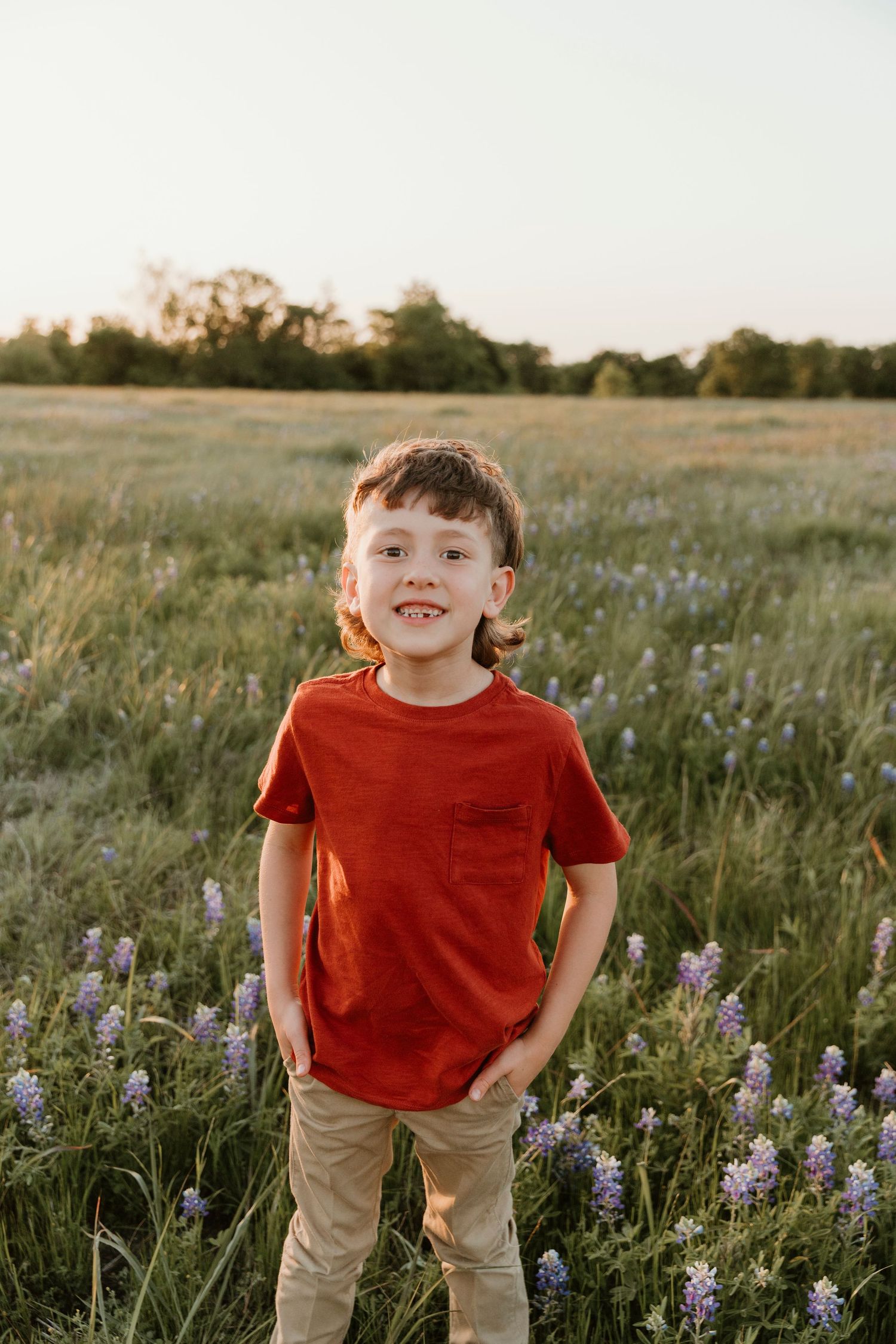 Child in red shirt standing among purple wildflowers during golden hour.