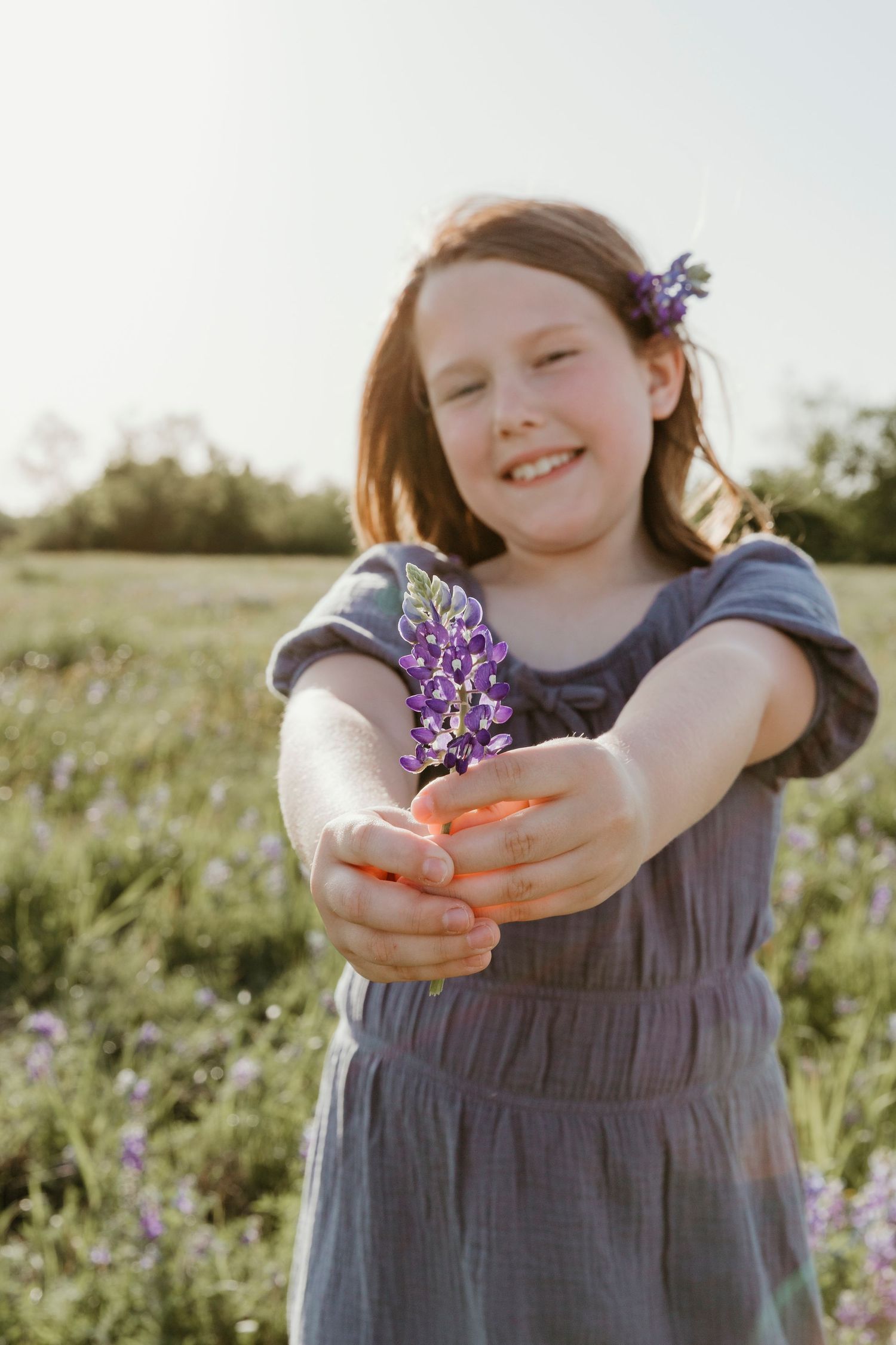 Sunny outdoor portrait with purple wildflower being held out towards camera.