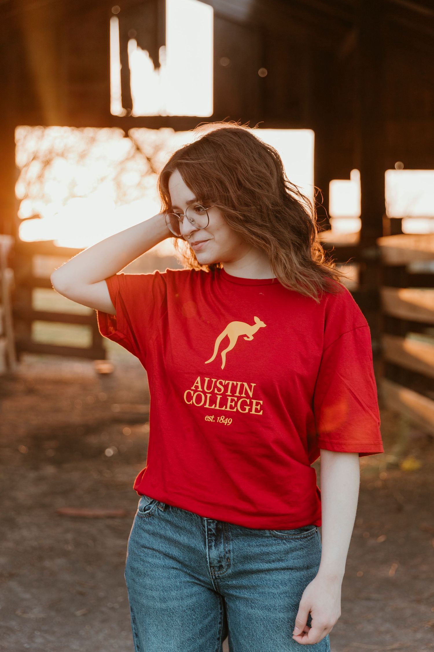 Student wearing Austin College t-shirt poses in warm sunset lighting.