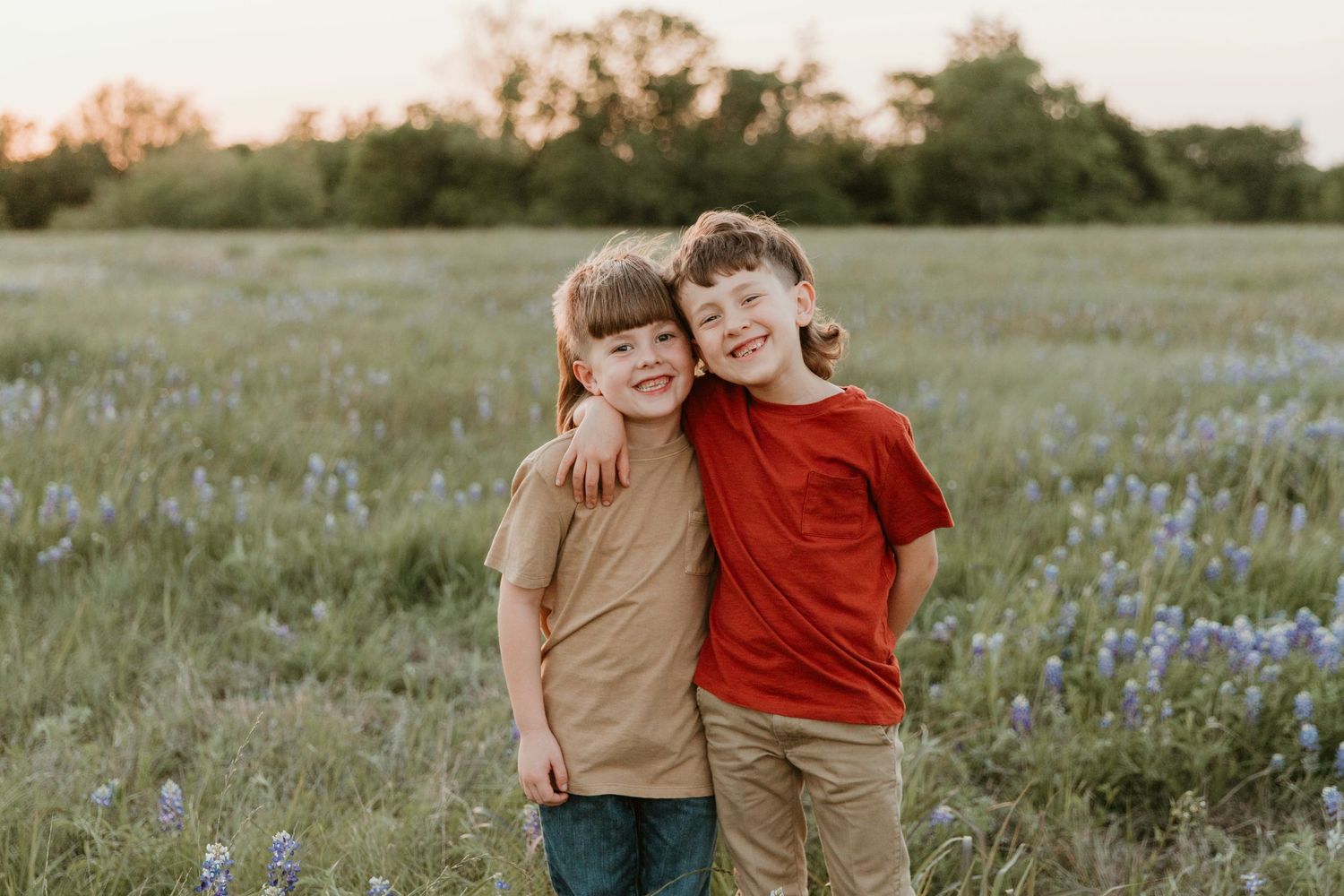 Candid shots of siblings playing and laughing in a wildflower meadow at sunset.