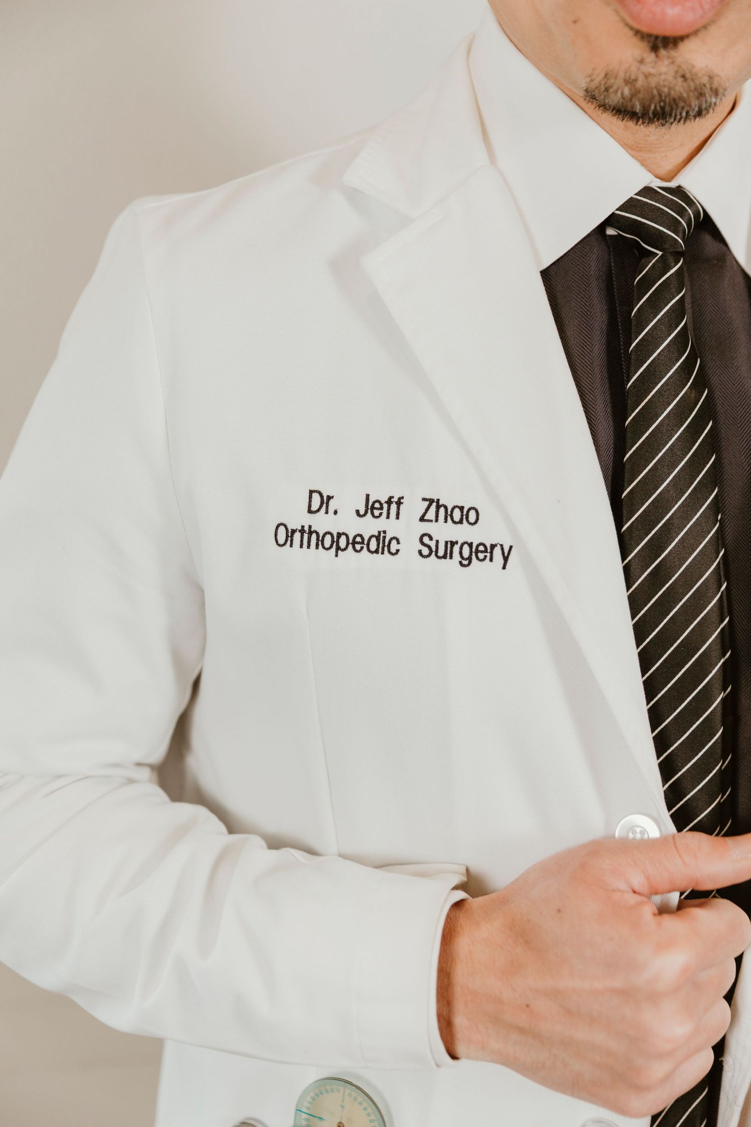 White medical coat with Dr. Jeff Zhao Orthopedic Surgery embroidered name tag and striped tie visible.