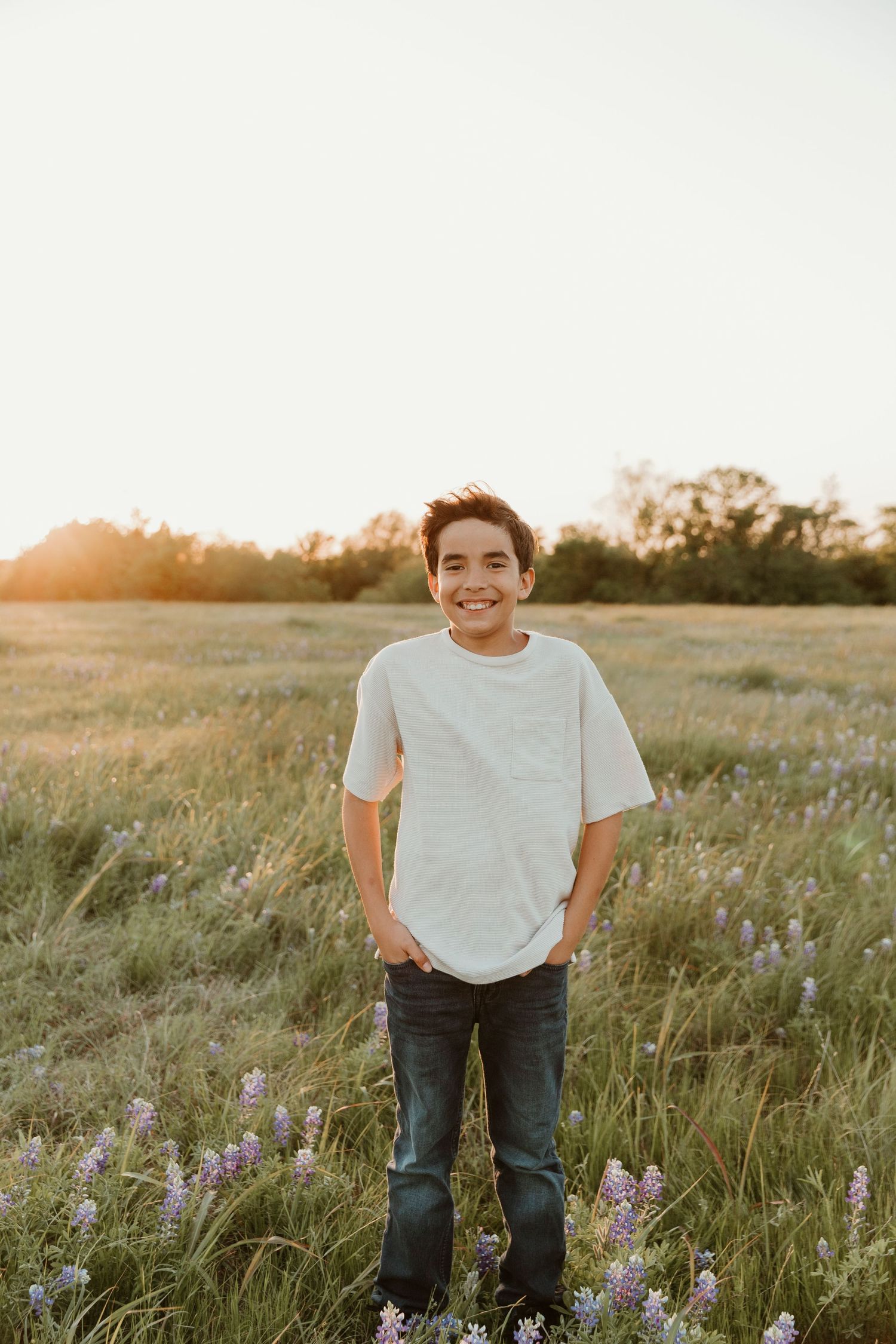 Teen in white t-shirt standing in field of wildflowers at sunset.