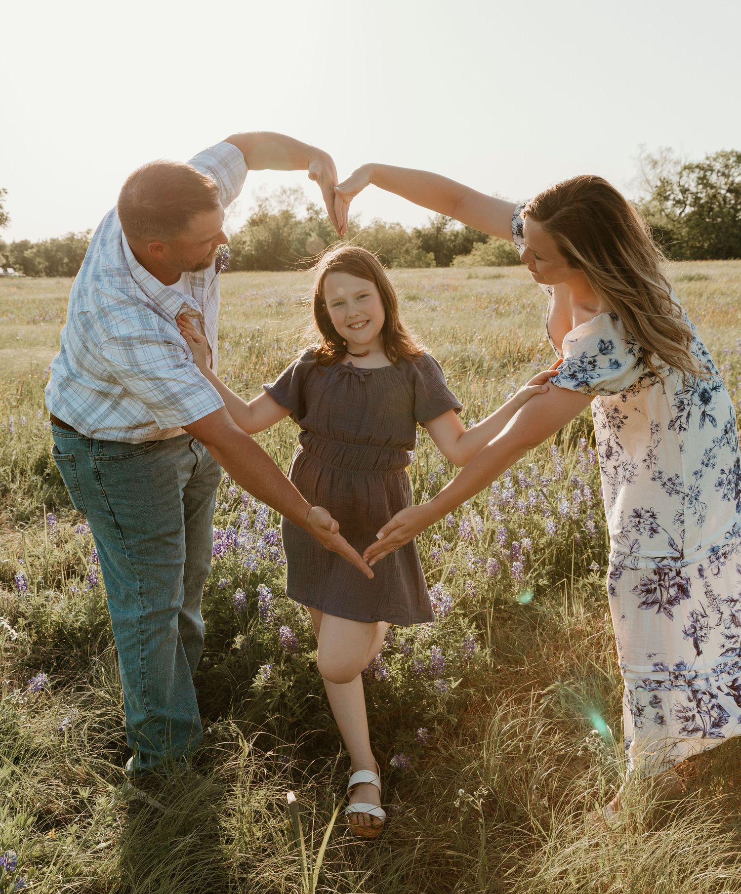 Family holding hands in a circle in a sunny meadow with wildflowers.