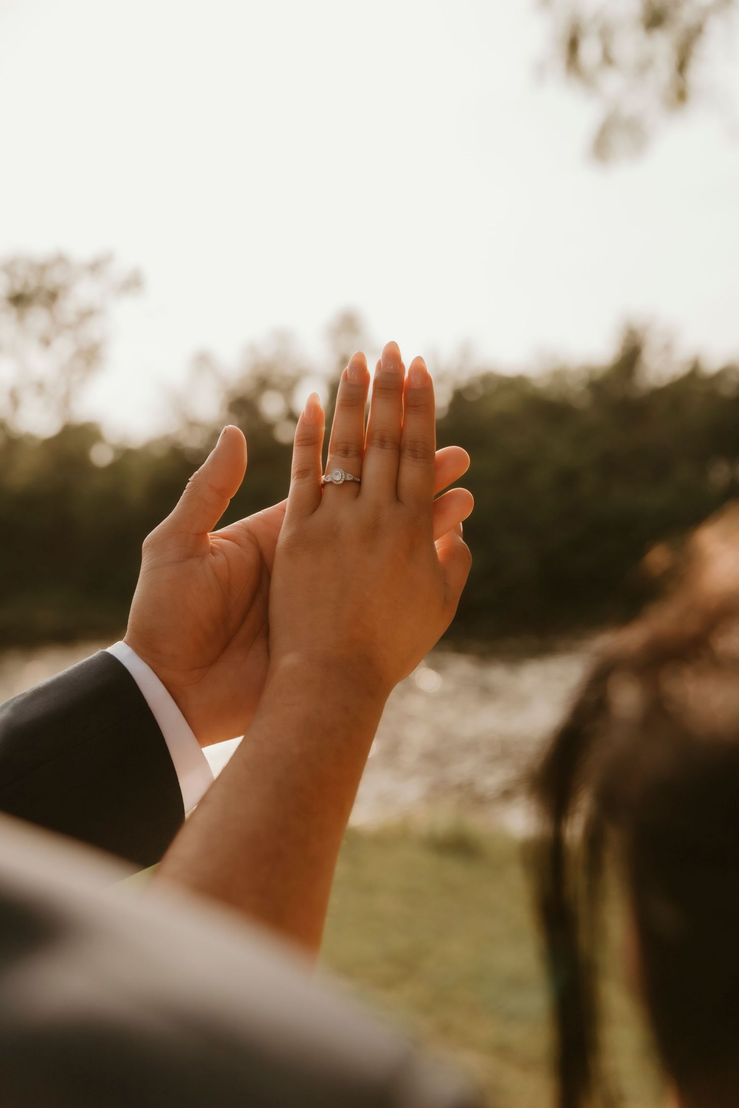 Silhouetted hands with engagement ring against golden sunset backdrop.