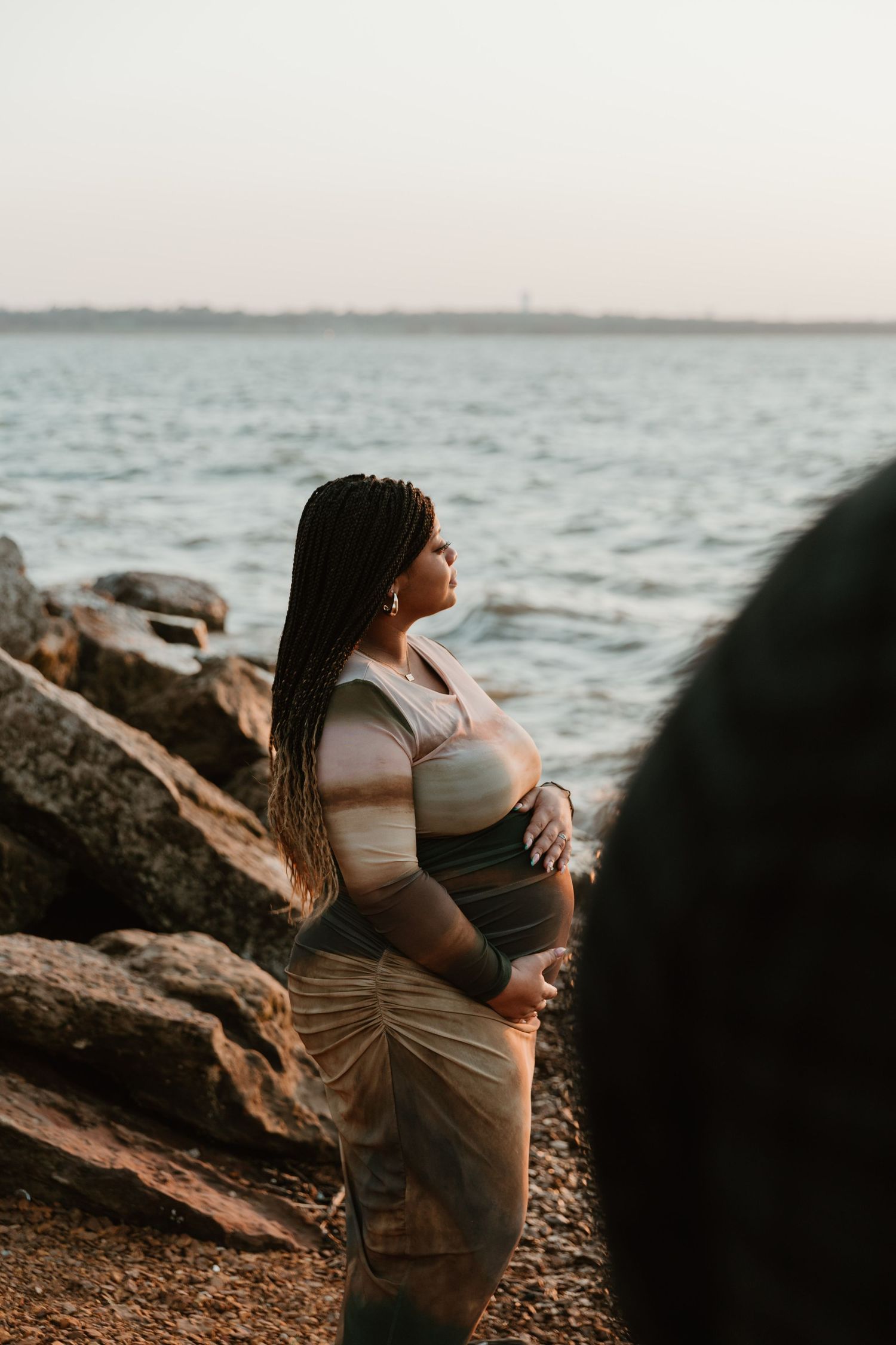 Side-profile maternity photo on rocky beach with setting sun.