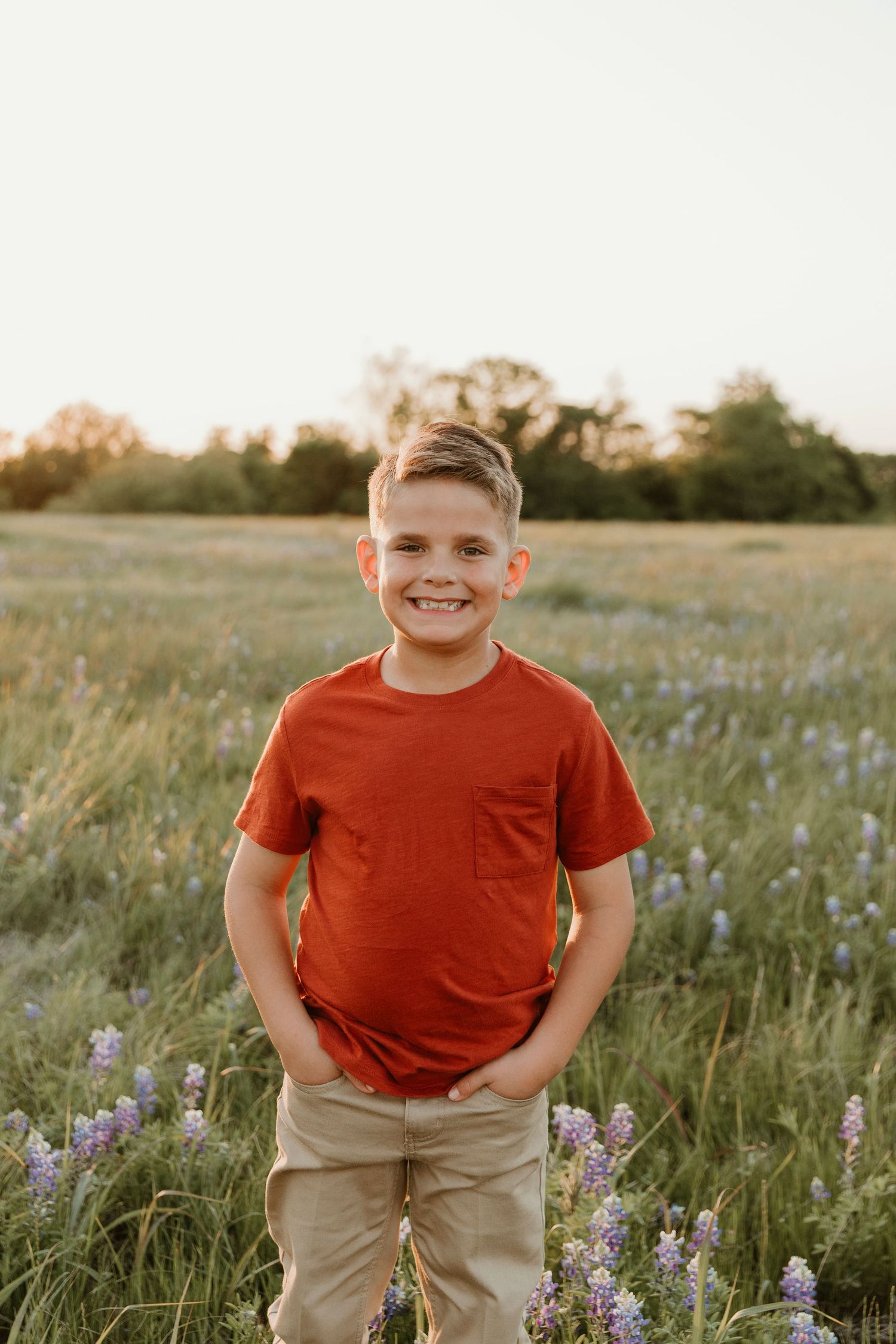 Young boy in red t-shirt smiling in a field of purple wildflowers at sunset.