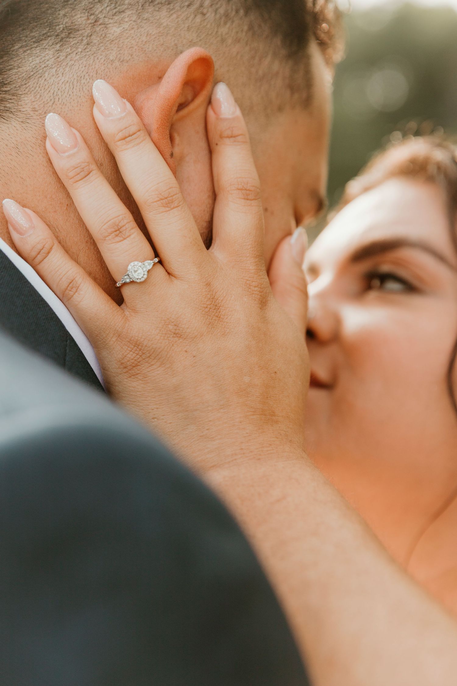 Close-up romantic moment at sunset showing bride's hand with engagement ring.