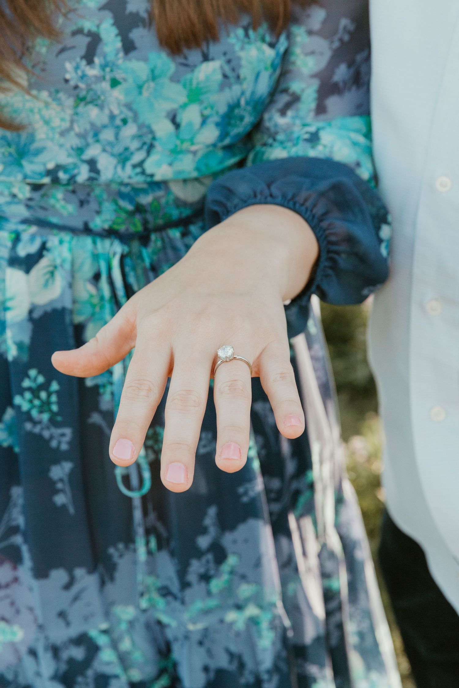 Close-up shots of engagement ring on hand with floral dress in background.