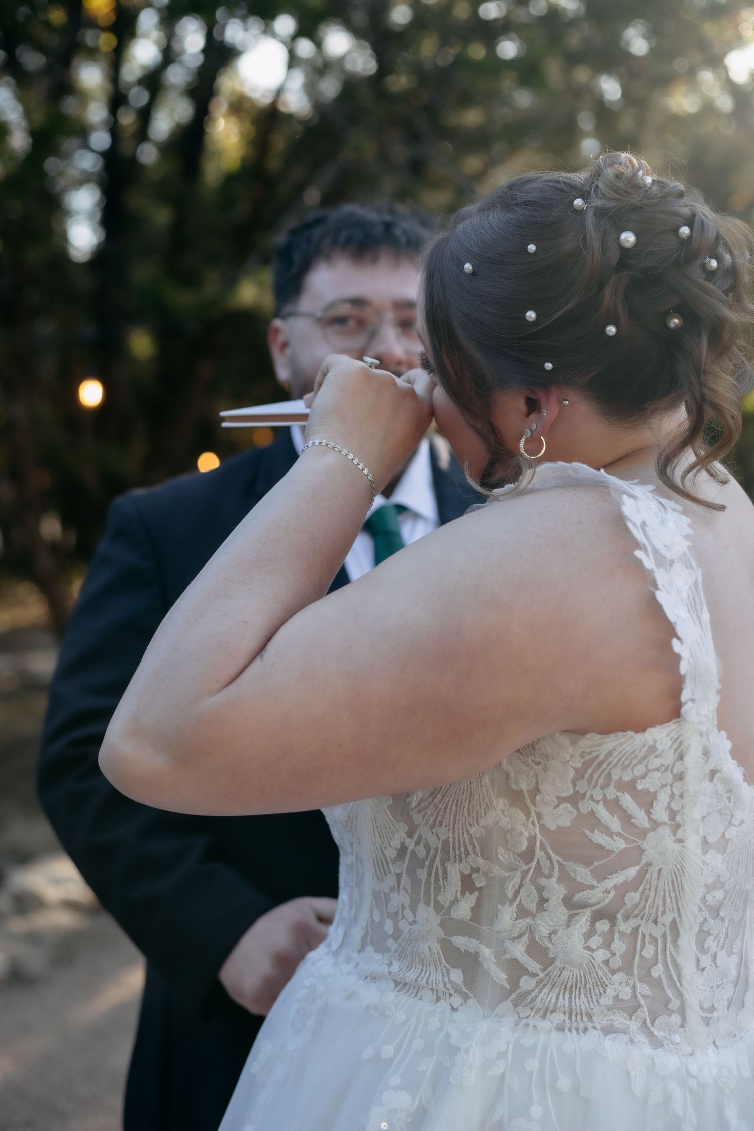 Side view of bride in detailed white wedding gown during outdoor ceremony.