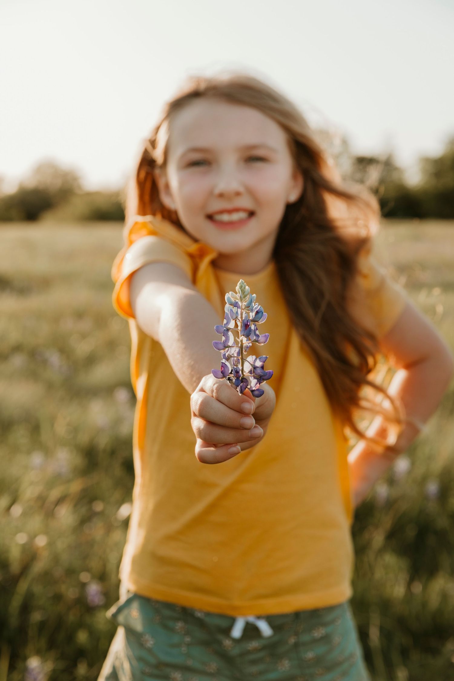 Bright outdoor scene with yellow shirt and extended arm holding purple wildflower.