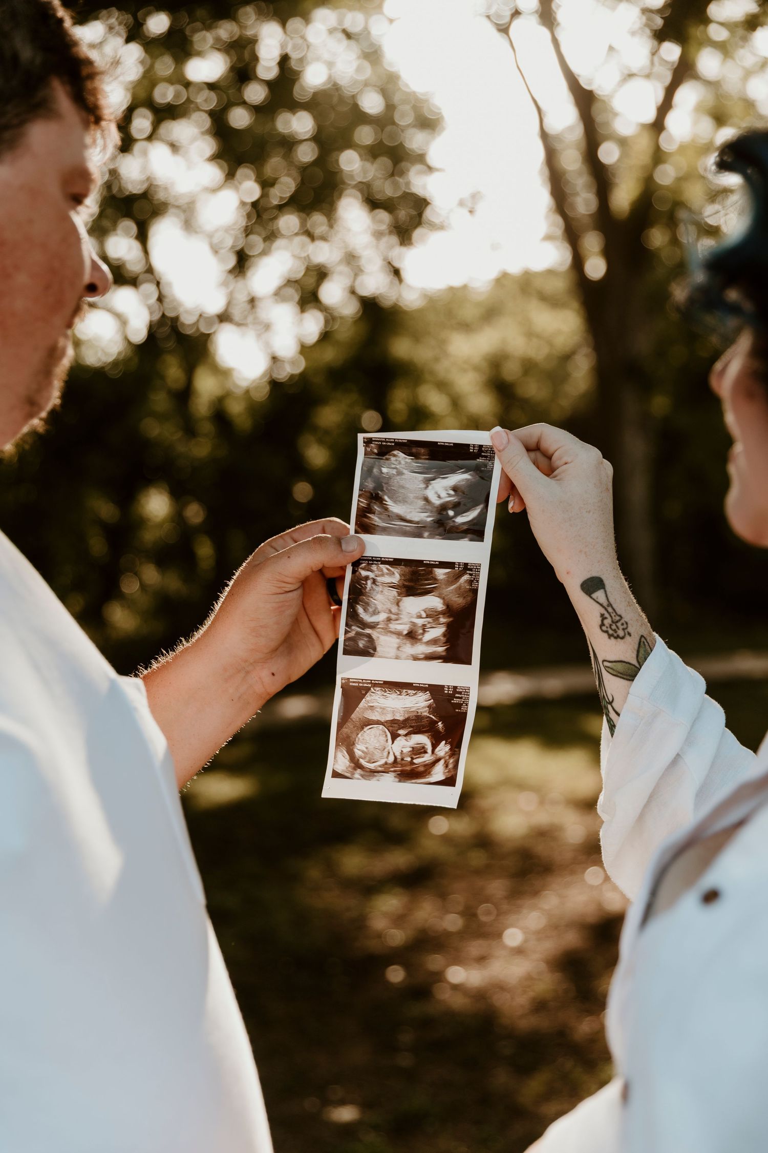 Hands holding ultrasound photos against a golden bokeh background during sunset.