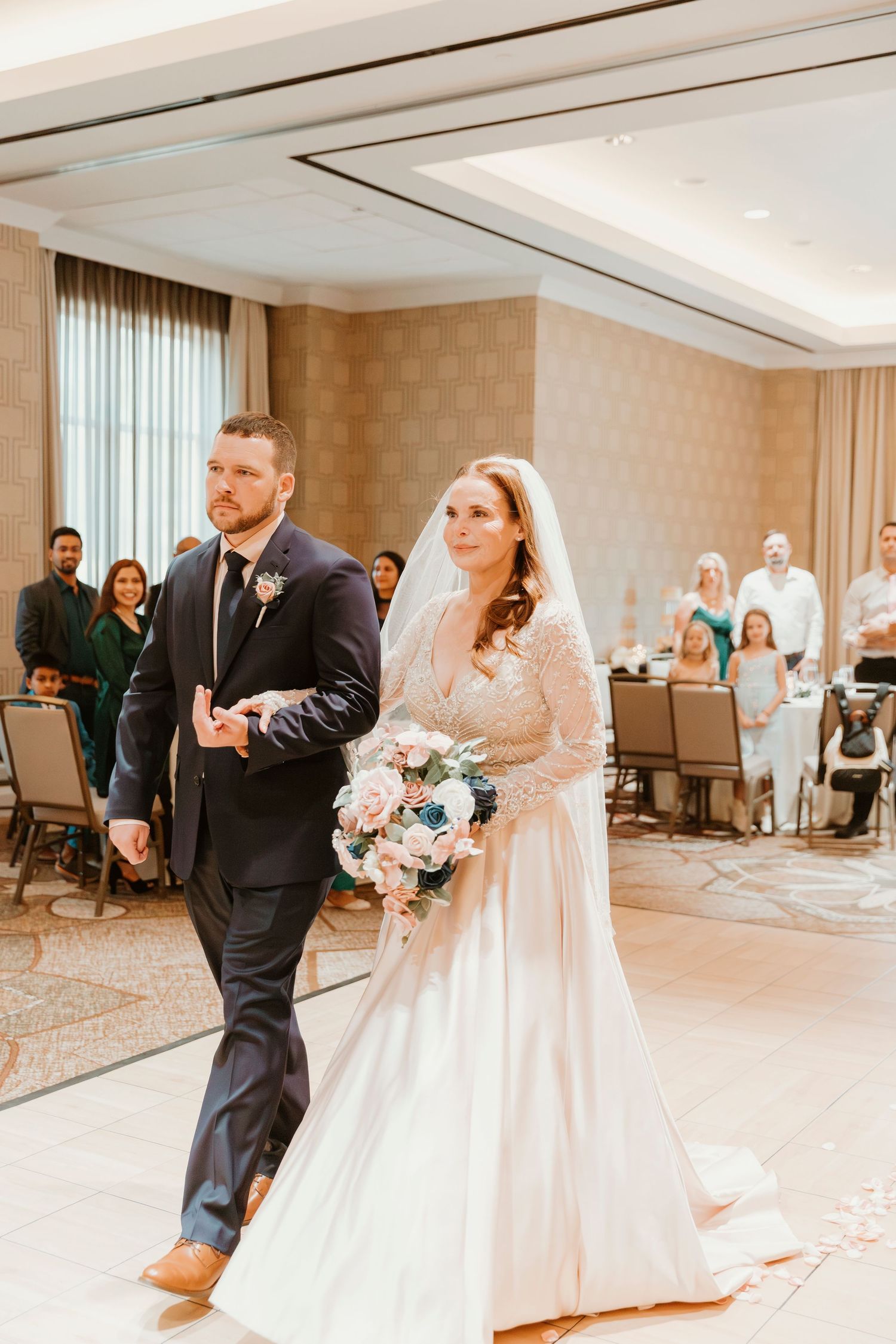 Newlyweds sharing their first dance together in an elegant ballroom with soft lighting and carpeted floors.