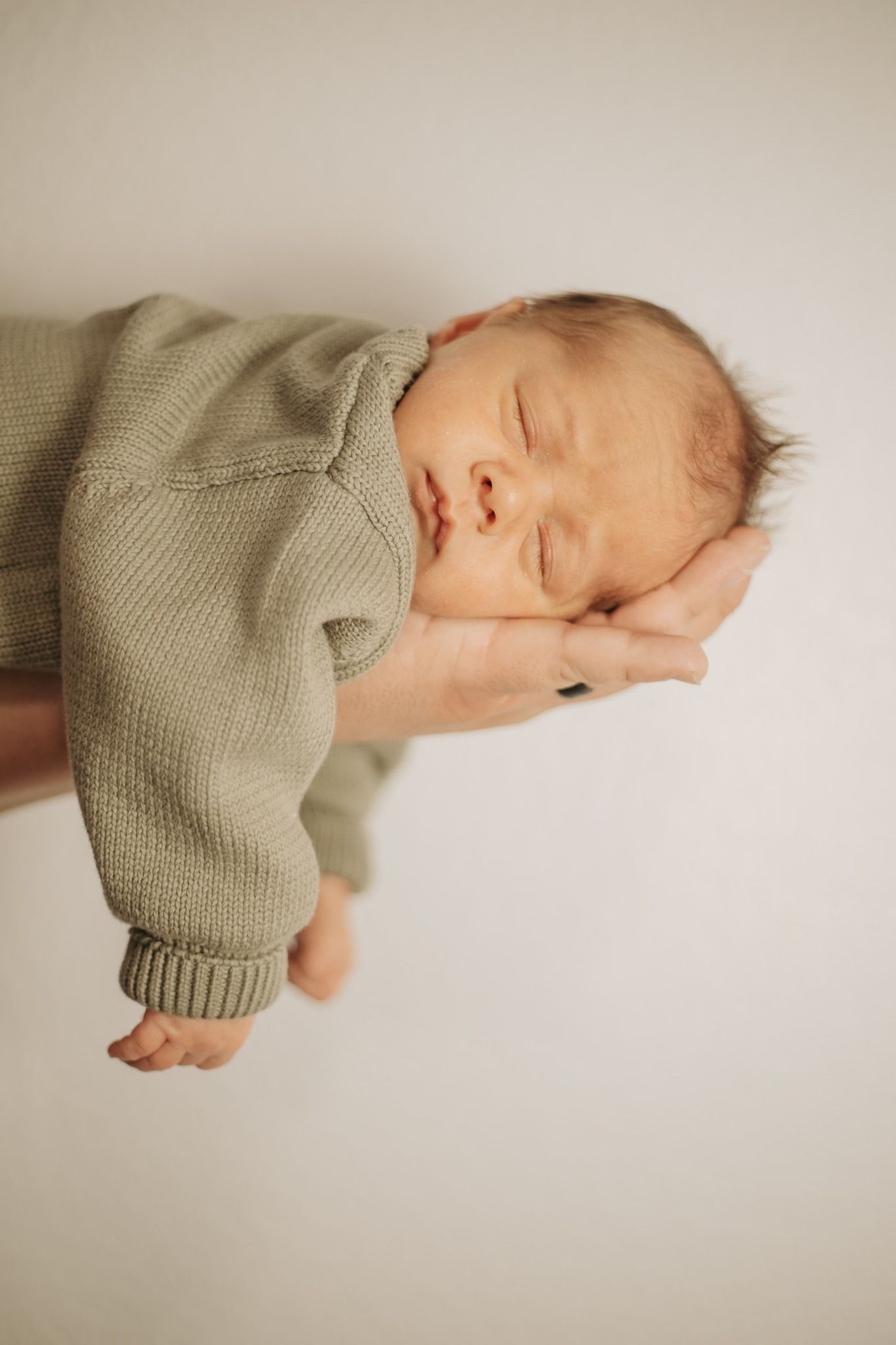 Peaceful sleeping newborn in gray knit sweater held in caring hands.