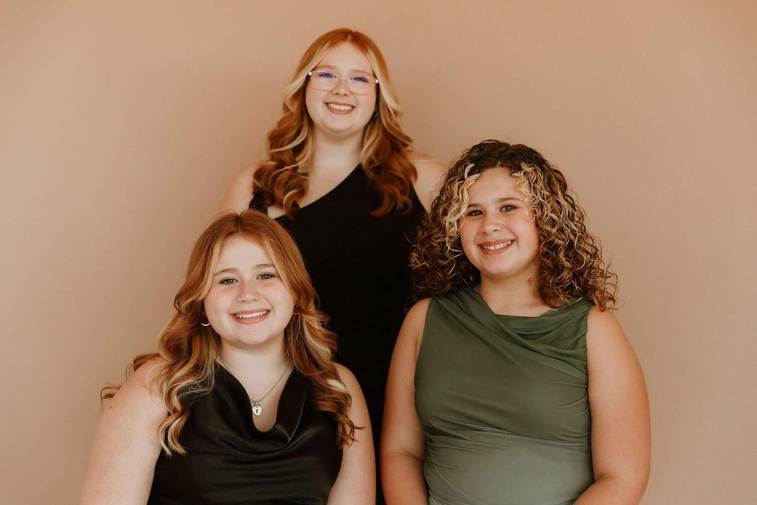 Three people with curly hair wearing black and green tops pose against a neutral background while smiling warmly.