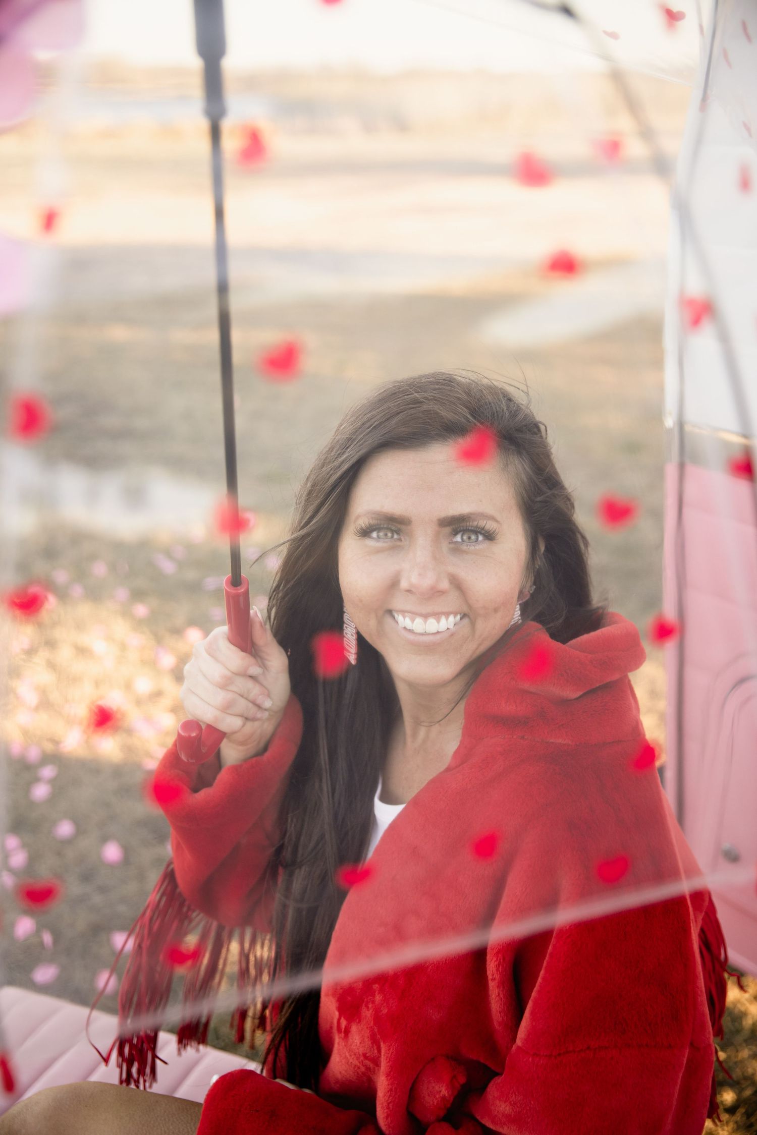 Woman in red coat holding umbrella with falling red petals in dreamy outdoor portrait.