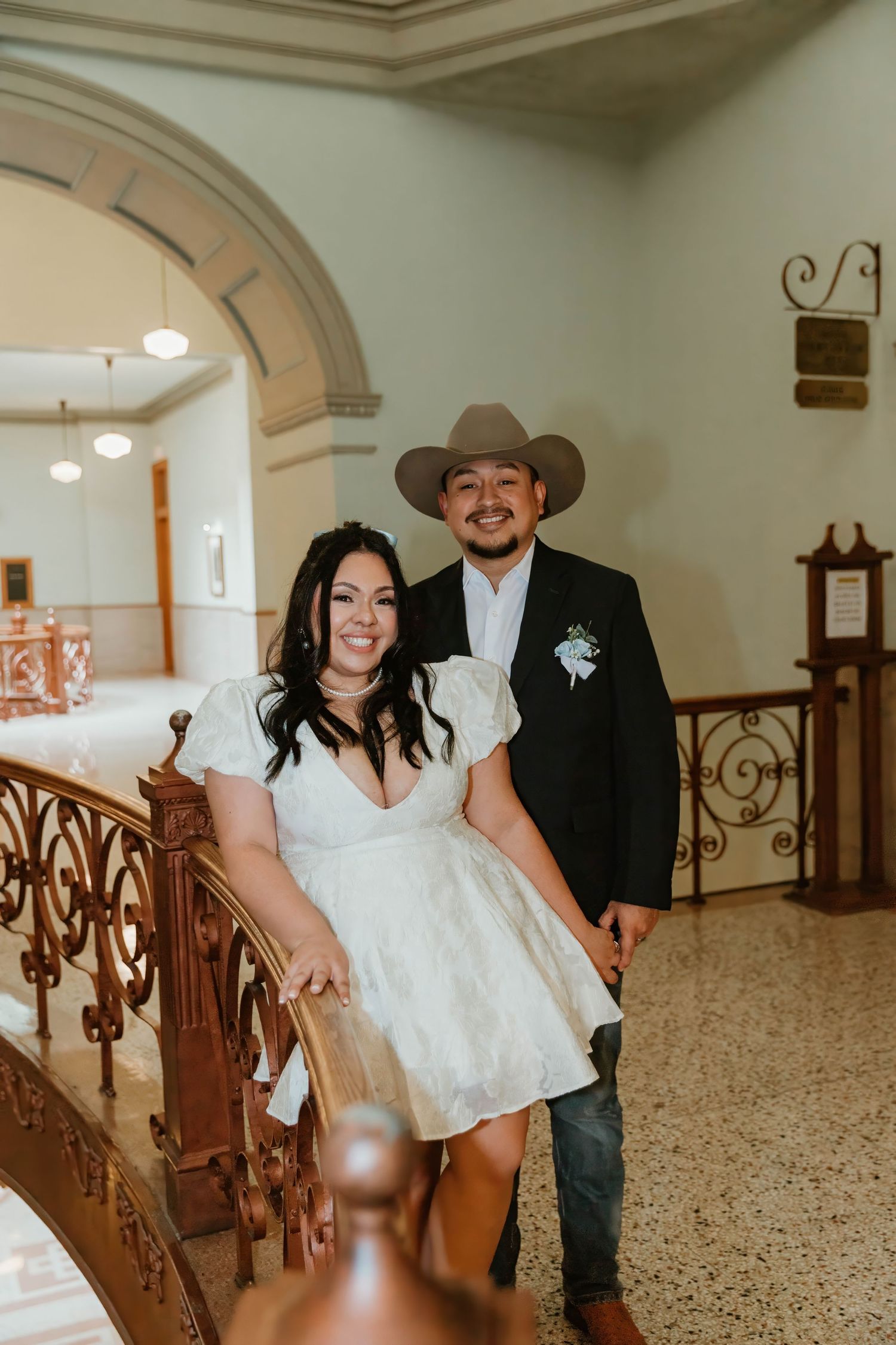 Wedding couple poses near elegant staircase in historic building interior.