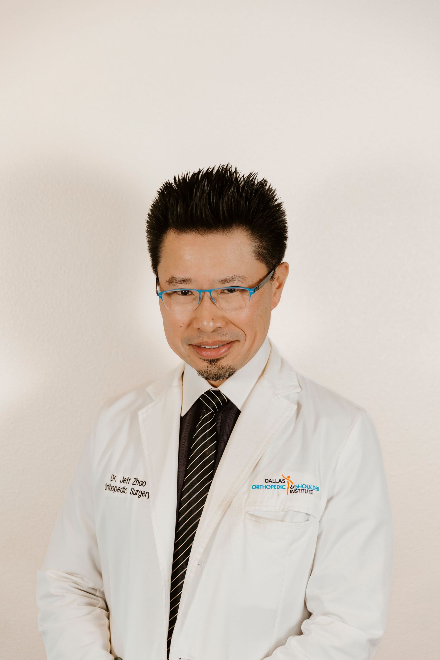 Healthcare professional in white coat and glasses poses for professional headshot.