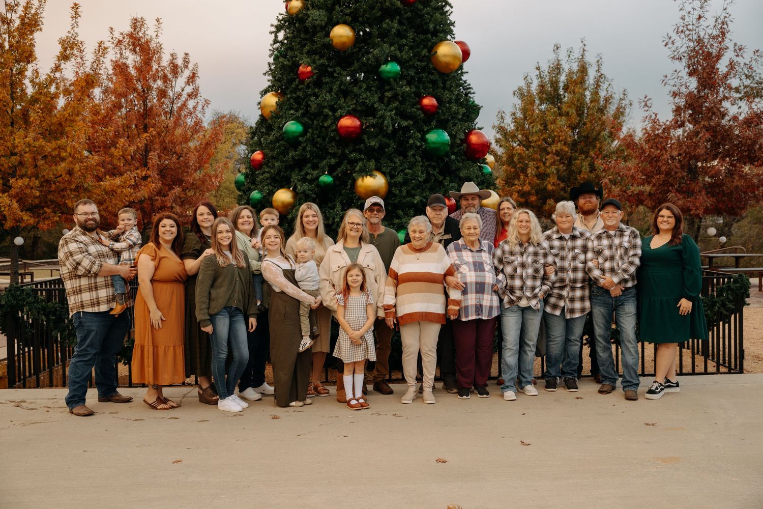 Family gathering outdoors with a decorated Christmas tree visible in the background during fall season.