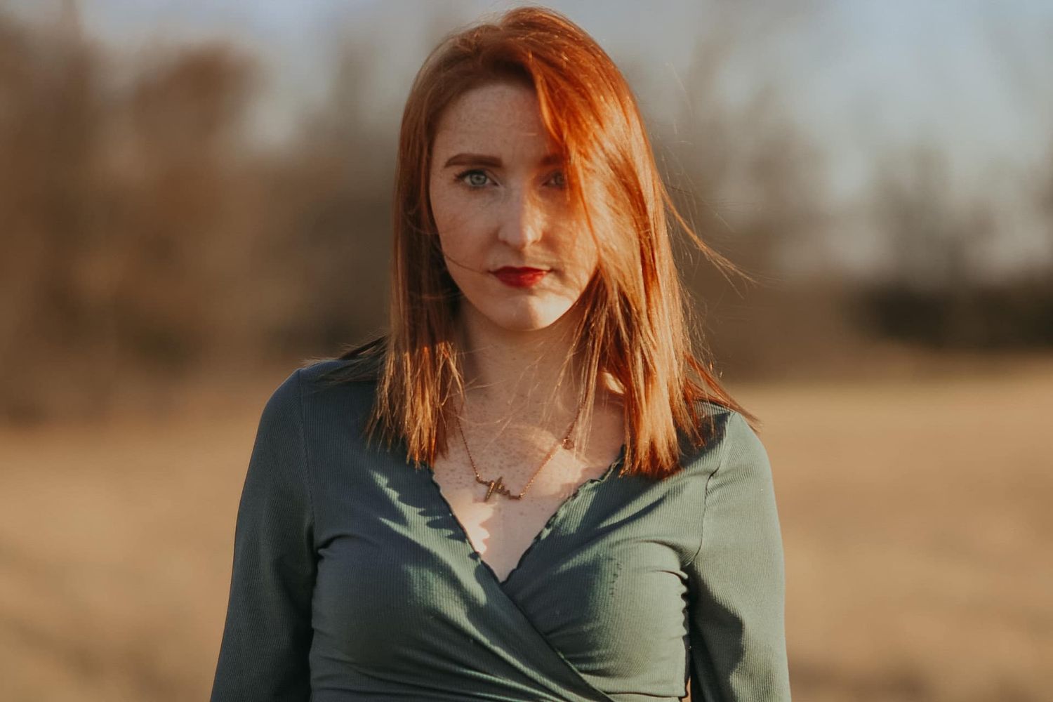 Close-up portrait in olive green top against natural outdoor lighting.