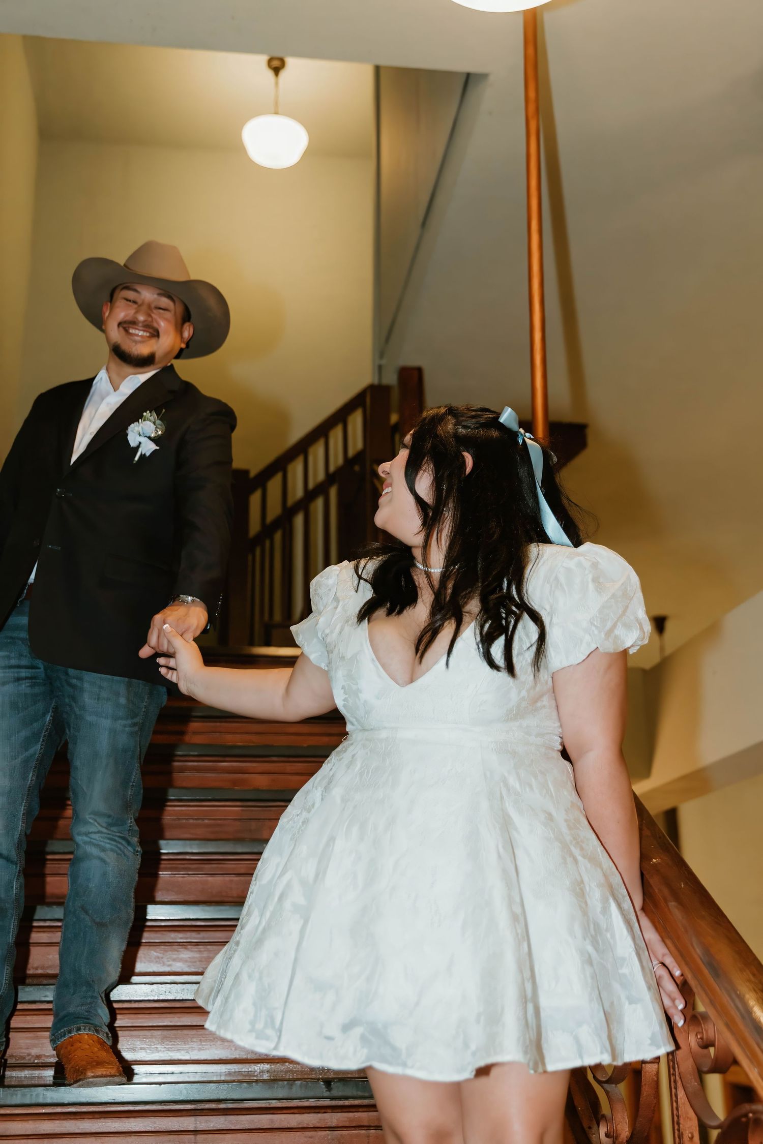 Couple descending ornate wooden staircase during wedding celebration.