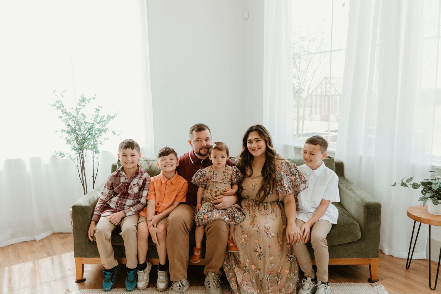 Family in coordinated outfits smiling while seated on modern green sofa in bright room.