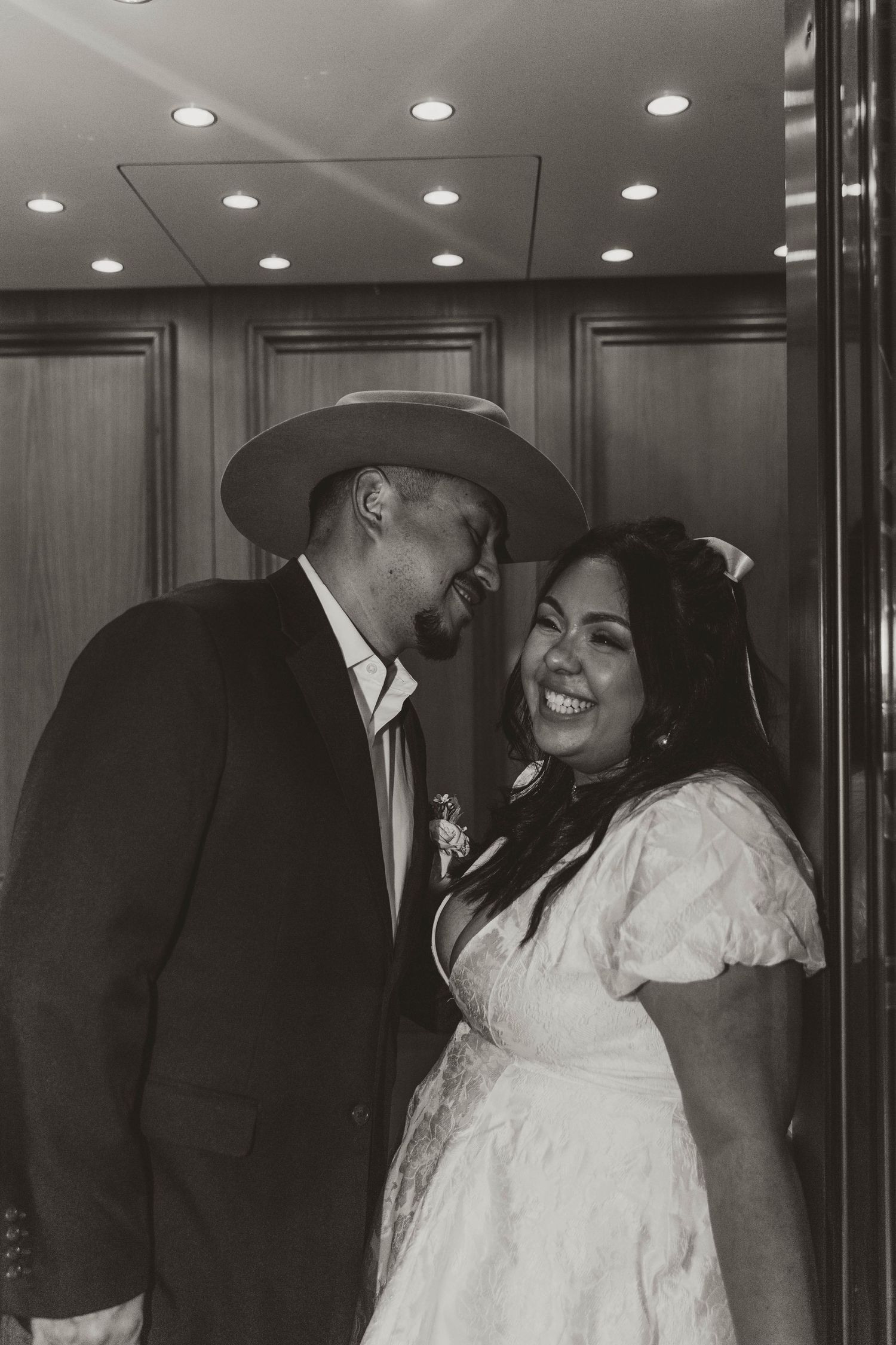 Black and white portrait of happy couple in wedding attire under recessed lighting.