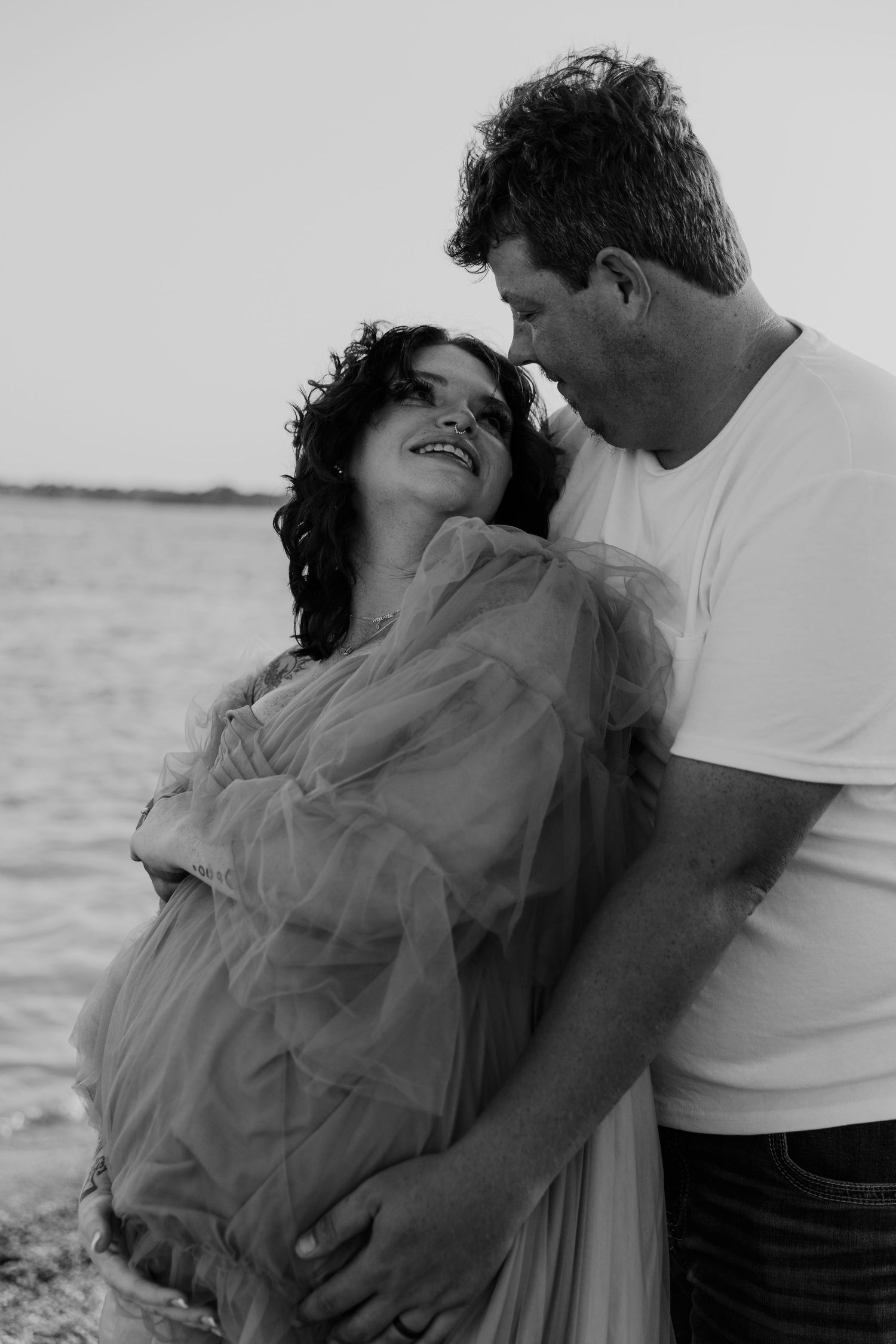 Black and white image of an intimate maternity photoshoot by the water.
