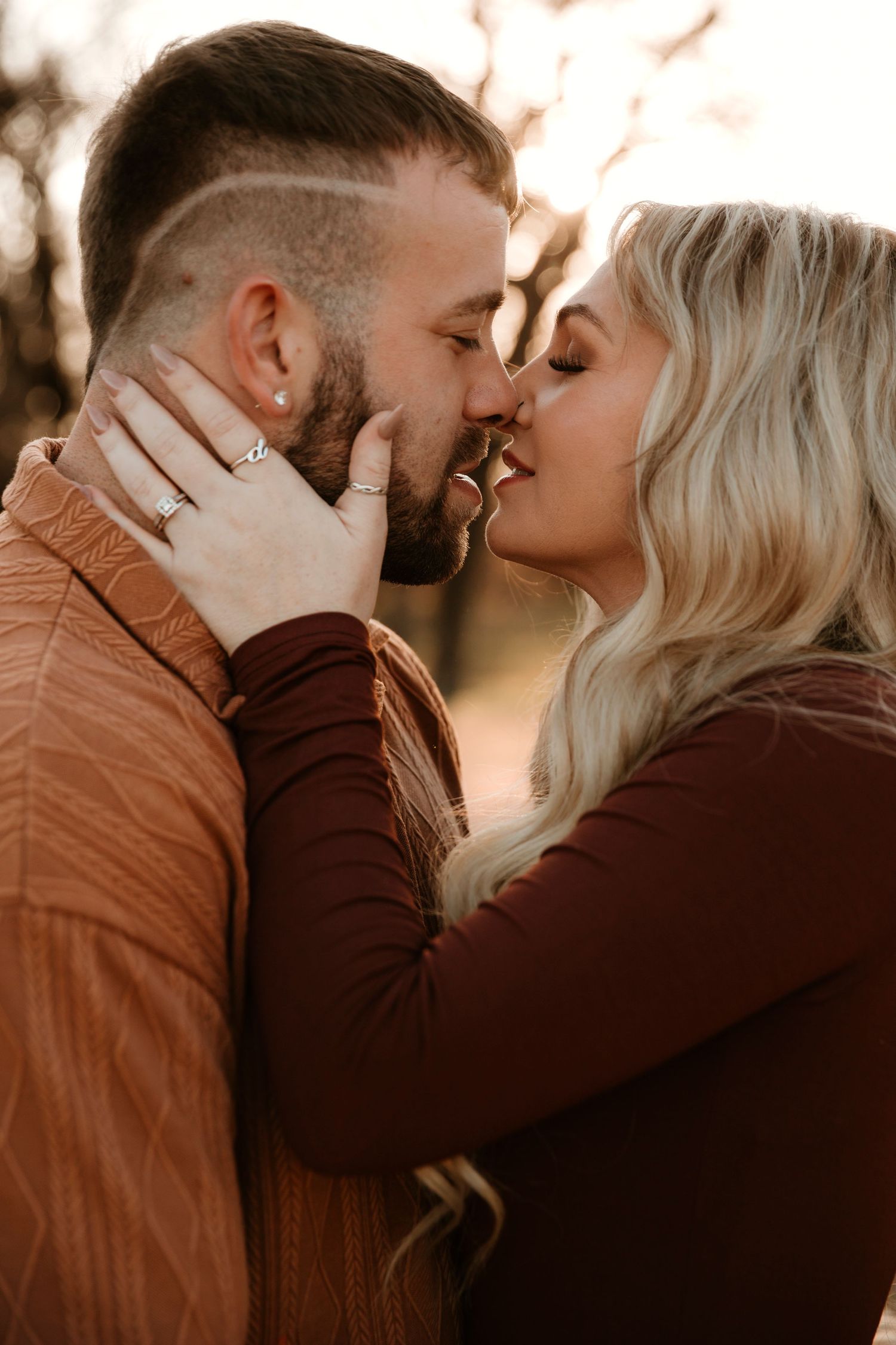 Romantic couple sharing intimate kisses in warm sunlight wearing brown and black outfits.