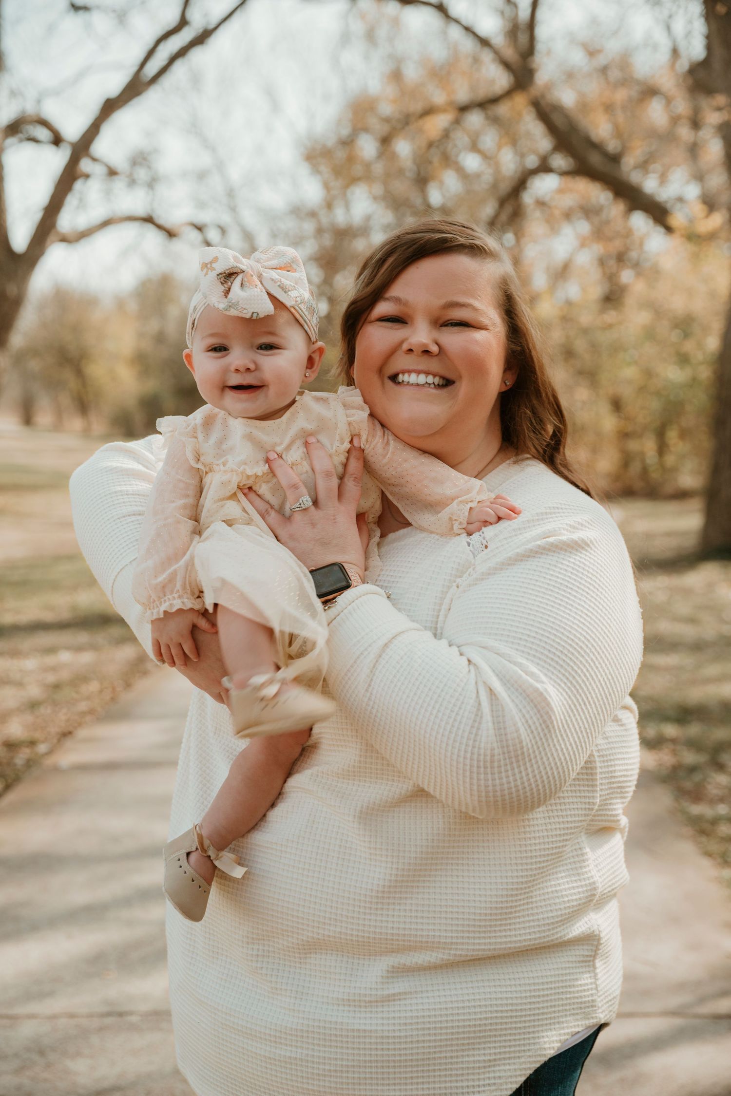 A heartwarming outdoor photoshoot shows tender moments between parent and baby in soft cream-colored sweaters.